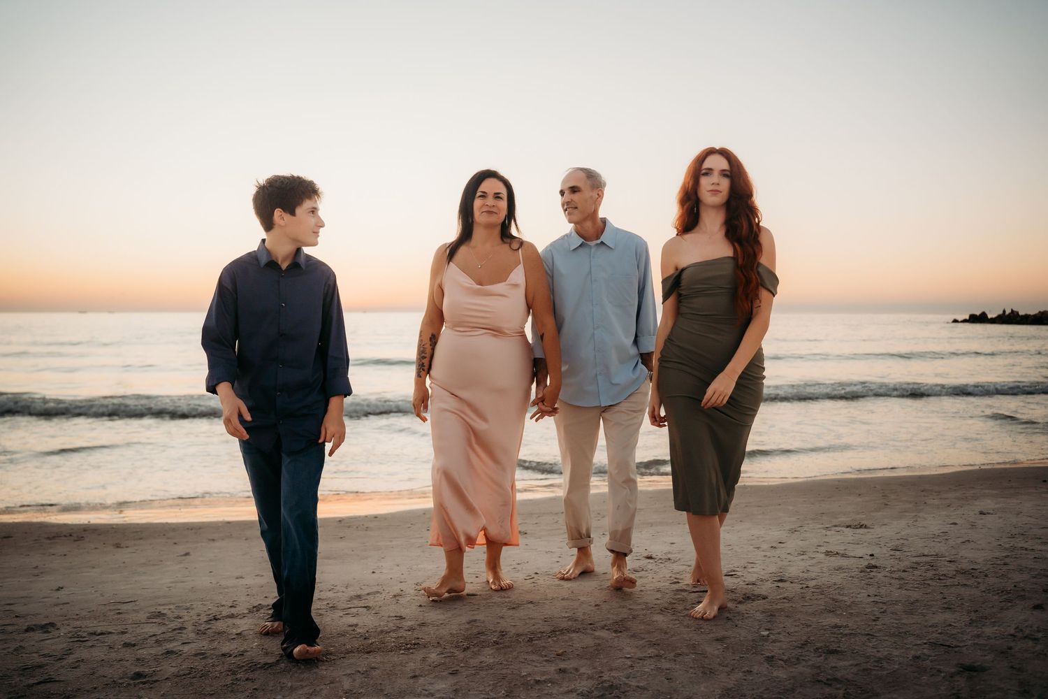 Family of four walking hand in hand along a scenic beach during a beautiful sunset.