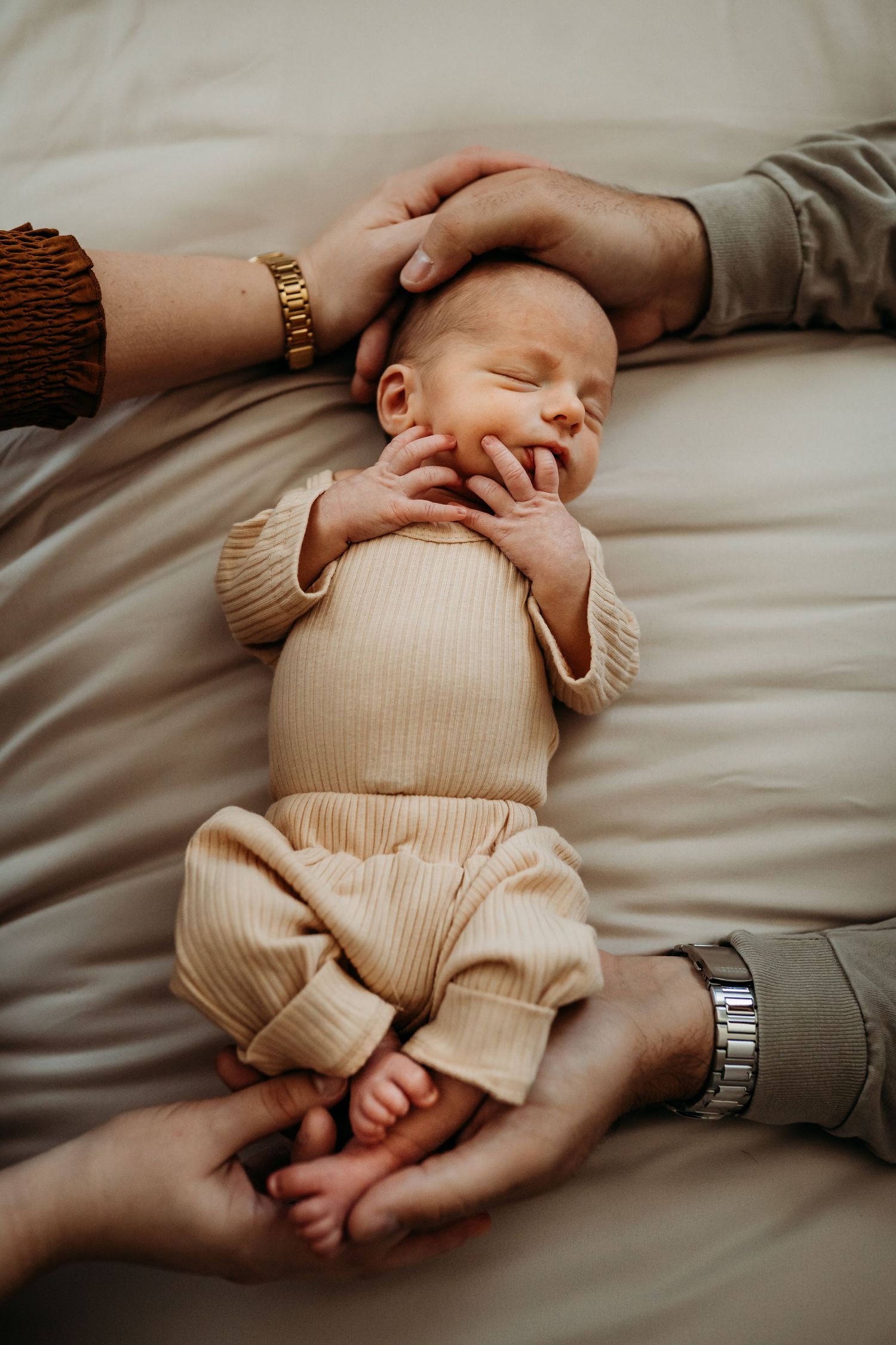 Sleeping newborn baby in beige outfit cradled by parents hands on soft bedding.