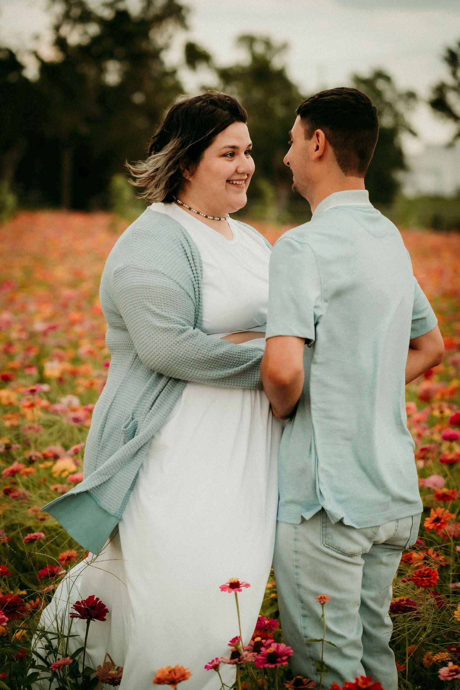 Couple embraces in vibrant flower field wearing matching light blue and white outfits.