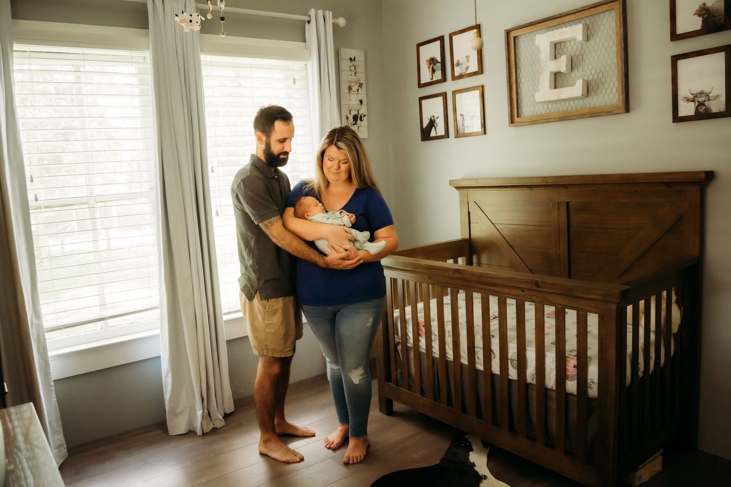 Happy parents standing beside wooden crib holding their newborn baby in nursery room.