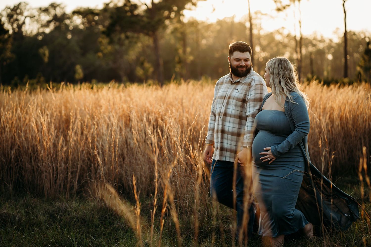 Expecting couple sharing a tender moment in a golden field at sunset during maternity shoot.
