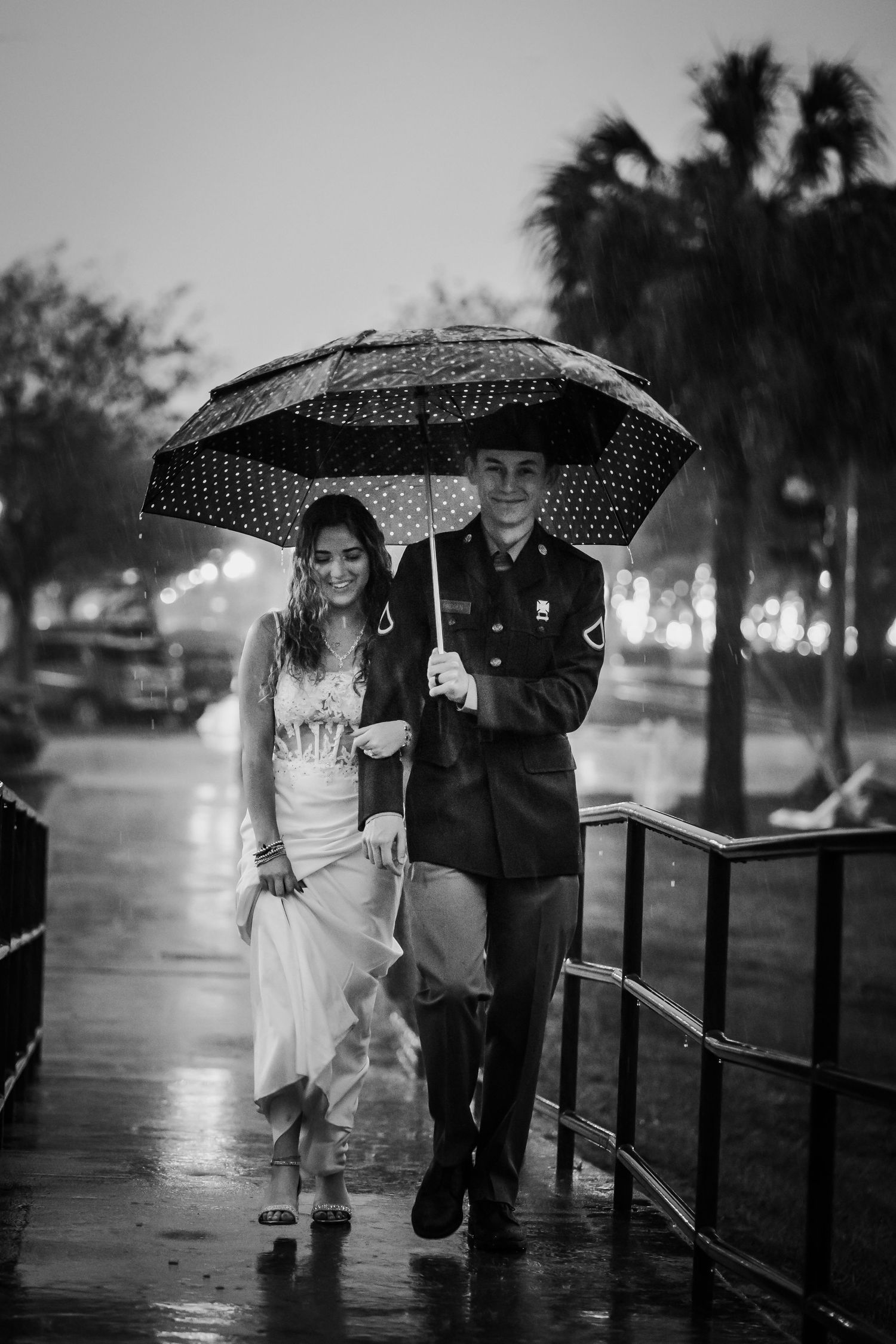 Black and white photo of a couple walking in the rain under a polka dot umbrella, man in military uniform.