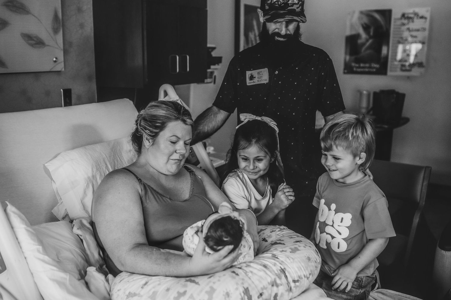 Black and white photo of mother in hospital bed holding newborn surrounded by family.