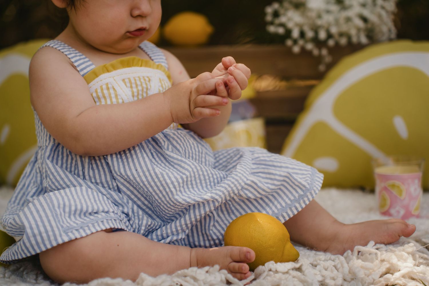 Baby girl in striped dress sitting on blanket with lemons, lemon-themed decorations in background.