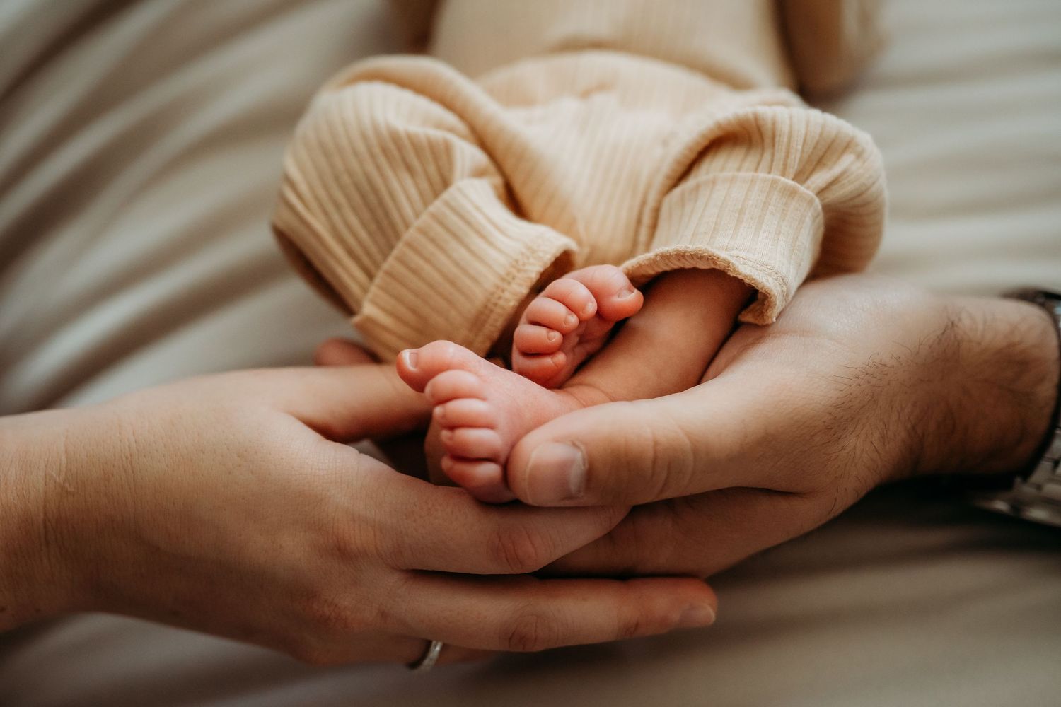 Parents gently cradling newborn baby's tiny feet in their hands, close-up detail shot.