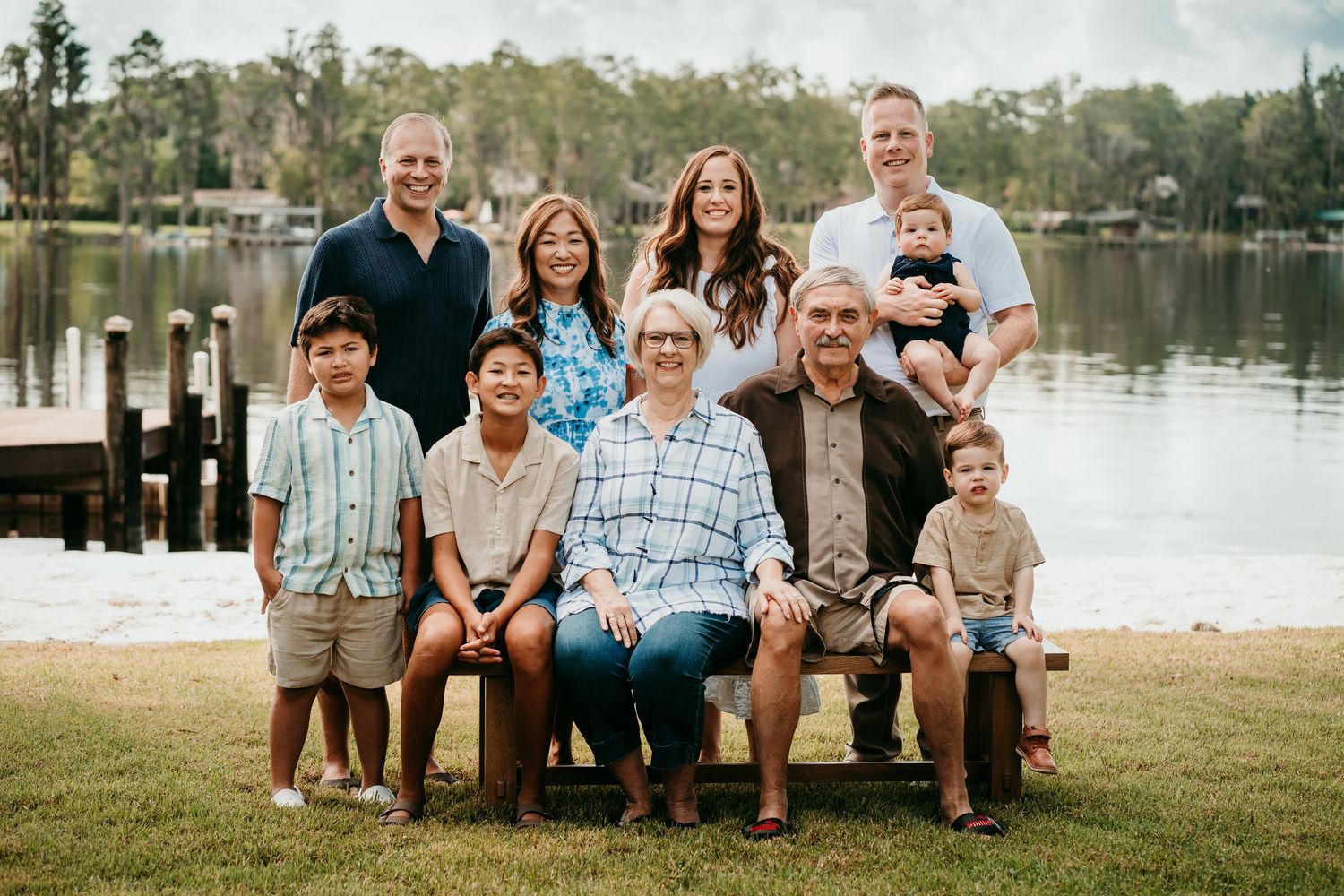 Extended multigenerational family posing together on a bench near a lake outdoors.