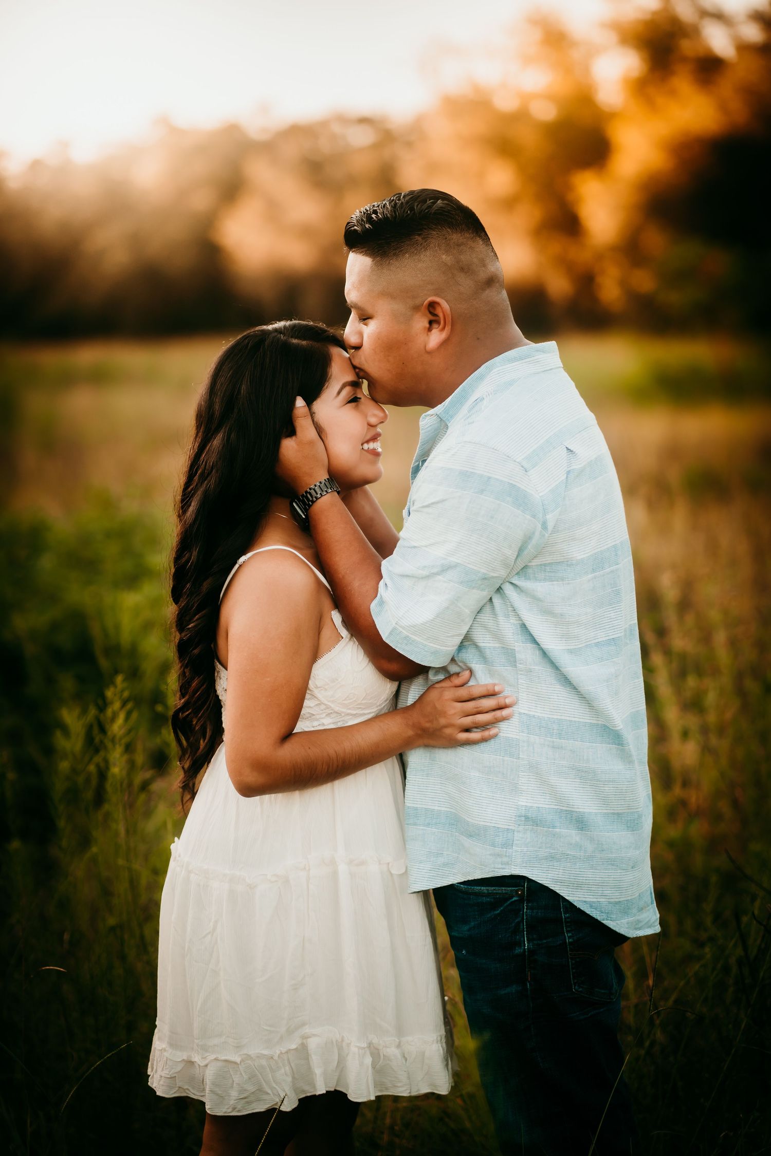 A couple shares a close romantic moment in a golden field at sunset, embracing and gazing at each other.