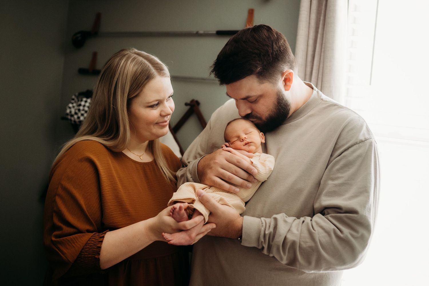 New parents smiling and cradling their newborn baby indoors in a warm, cozy setting.