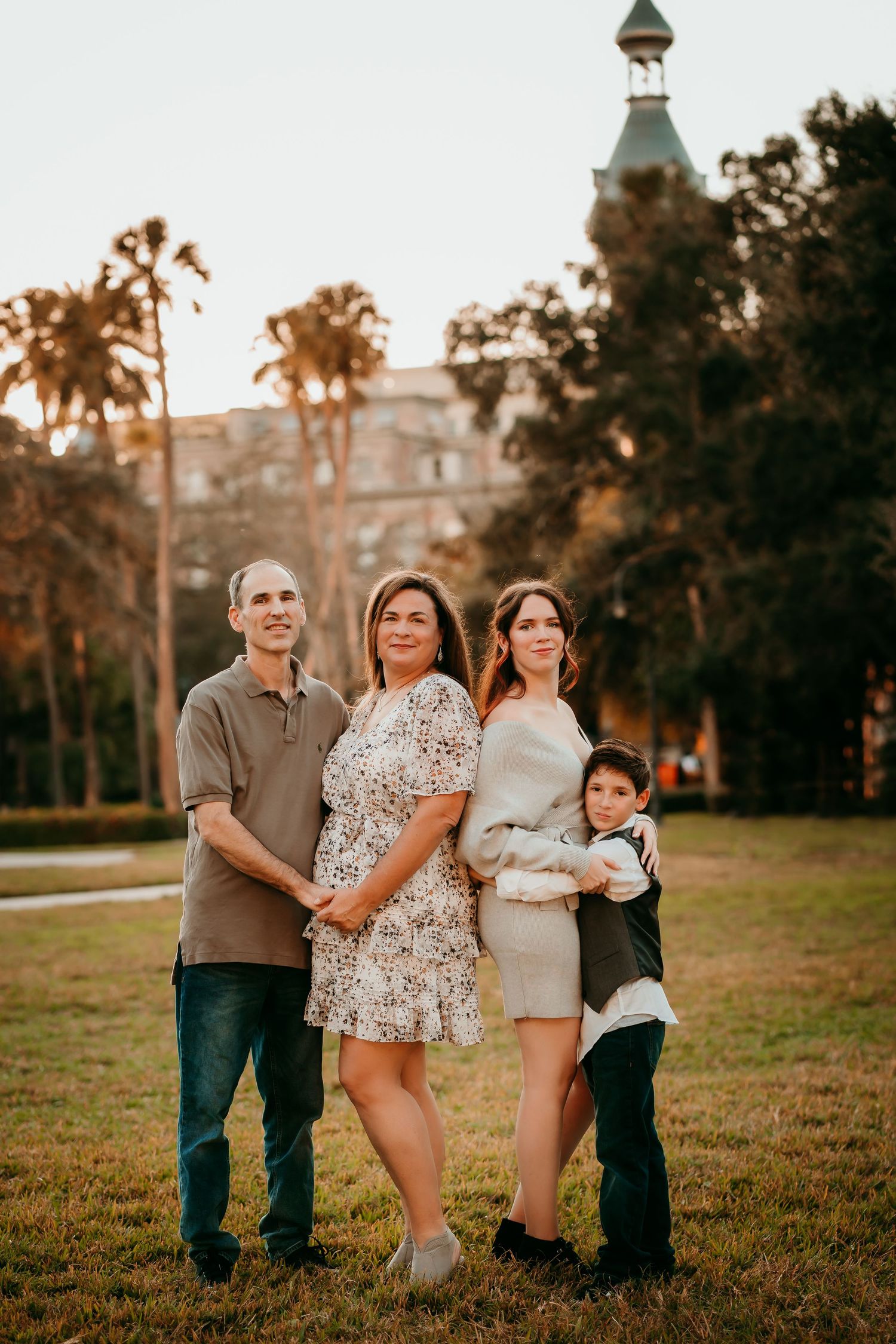 Family of four posing at sunset in a park with a historic building in the background.