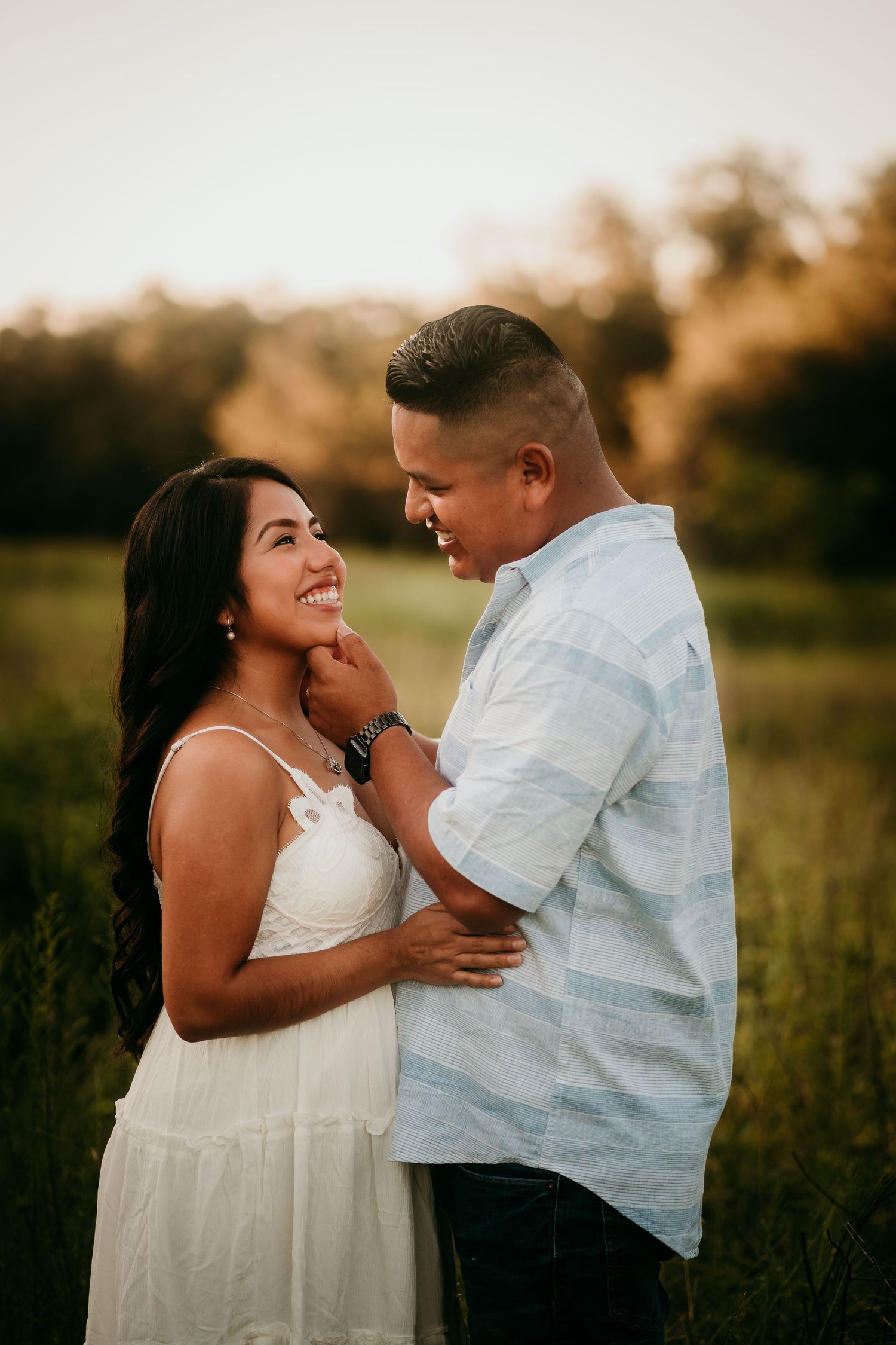 Smiling couple sharing a tender moment together in a lush green field at golden hour.