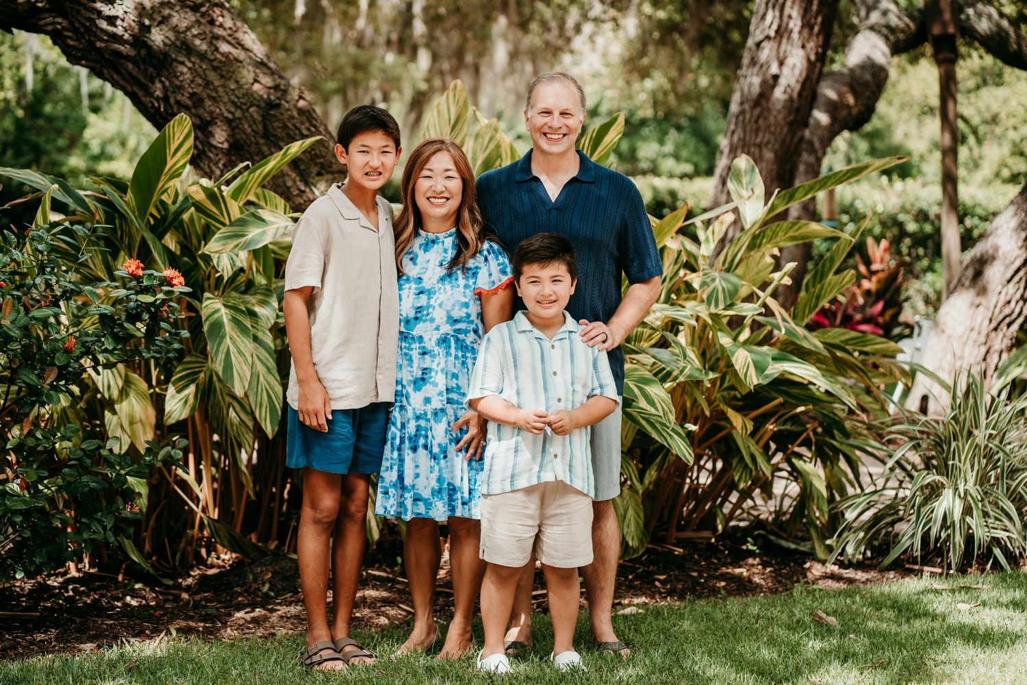 Happy family of four smiling together in front of vibrant tropical garden greenery.