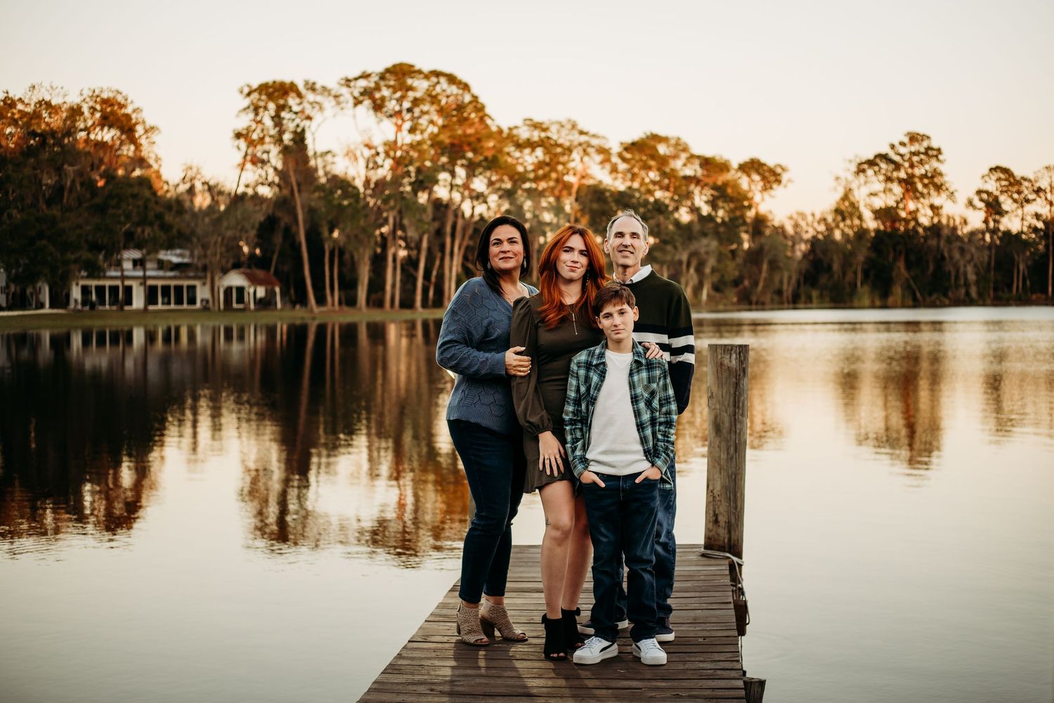 Family of four posing on wooden dock with lake at sunset.