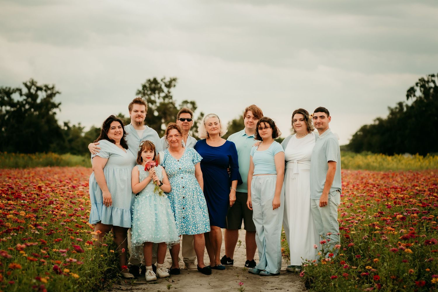 Family group portrait in a blooming red poppy field, wearing light blue and white outfits on a cloudy day.