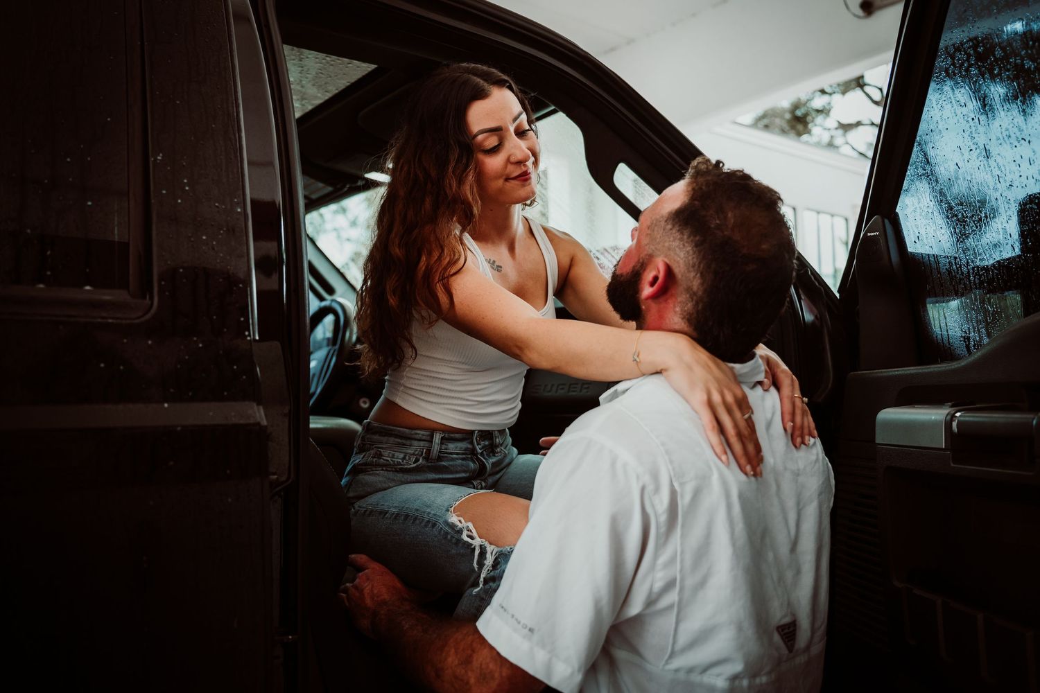 Couple sharing intimate moment in truck doorway, woman in white tank top and denim shorts.