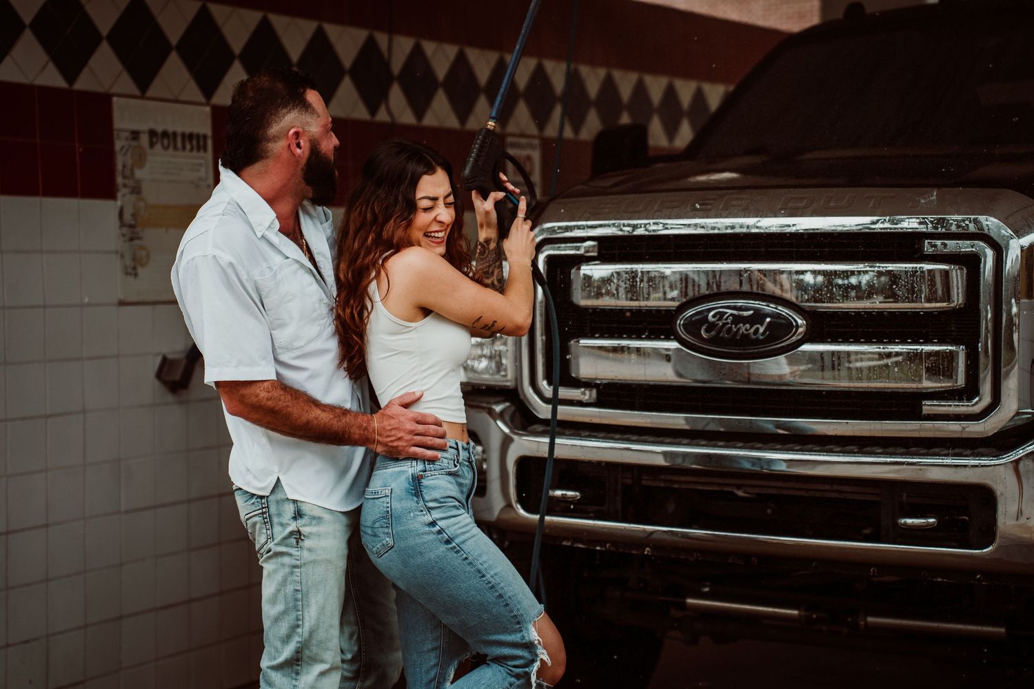 Couple embracing affectionately beside shiny black Ford truck in a car wash bay.