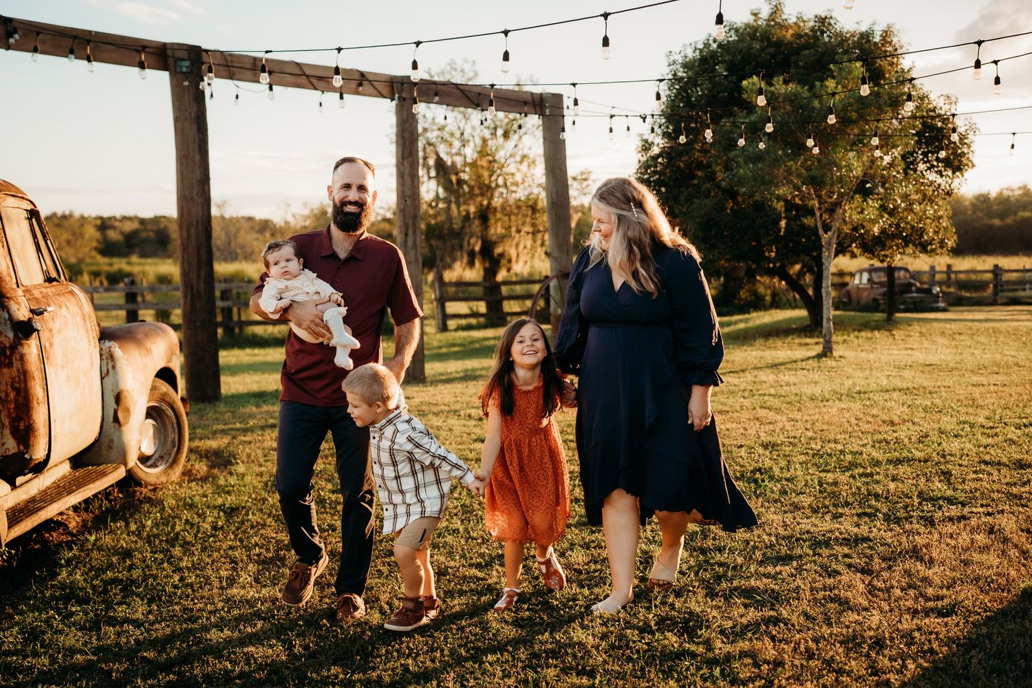 Family of five with three children walking on green farm lawn at golden hour.
