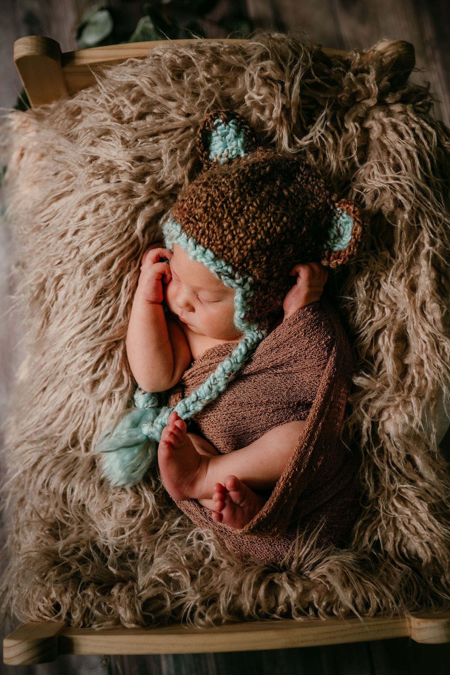 Newborn baby sleeping in brown knit bear hat and wrap on fluffy fur blanket.