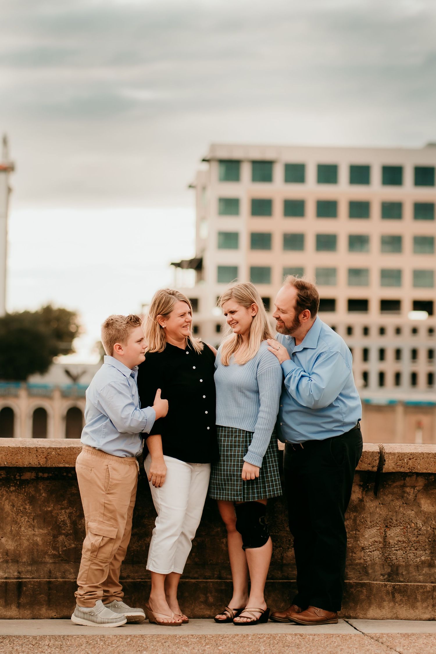Family of four smiling and posing together on a stone ledge with city buildings behind.