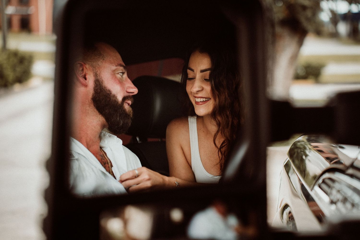 A couple smiles and laughs together inside a truck cab, captured through the window in warm light.
