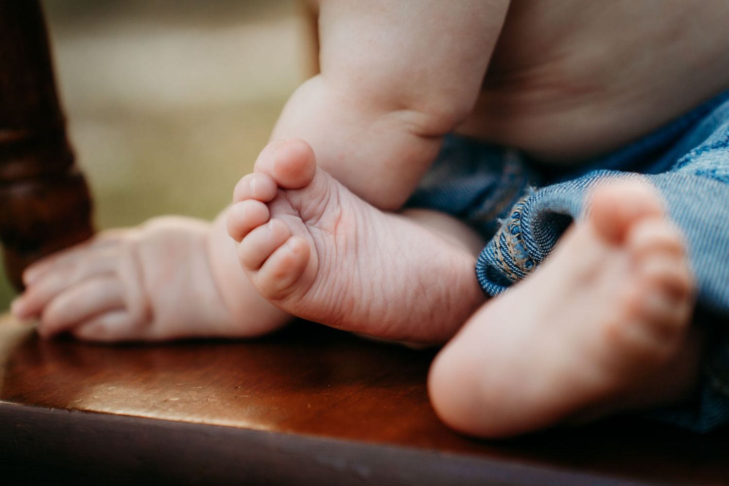 Close-up of cute baby feet resting on a wooden surface, wearing blue denim jeans.