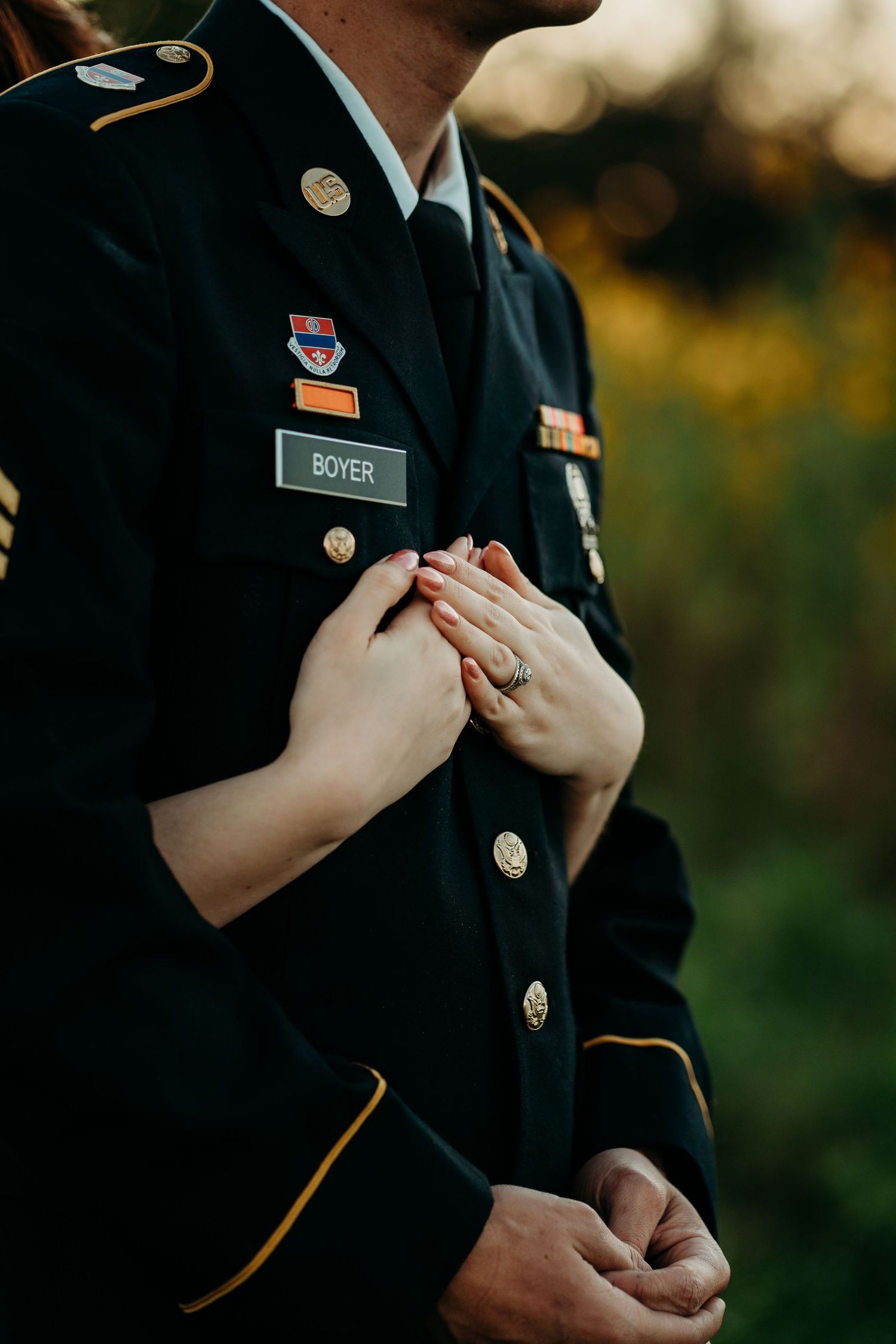 Close-up of woman's hand resting on soldier's chest, showing engagement ring on Army dress uniform.
