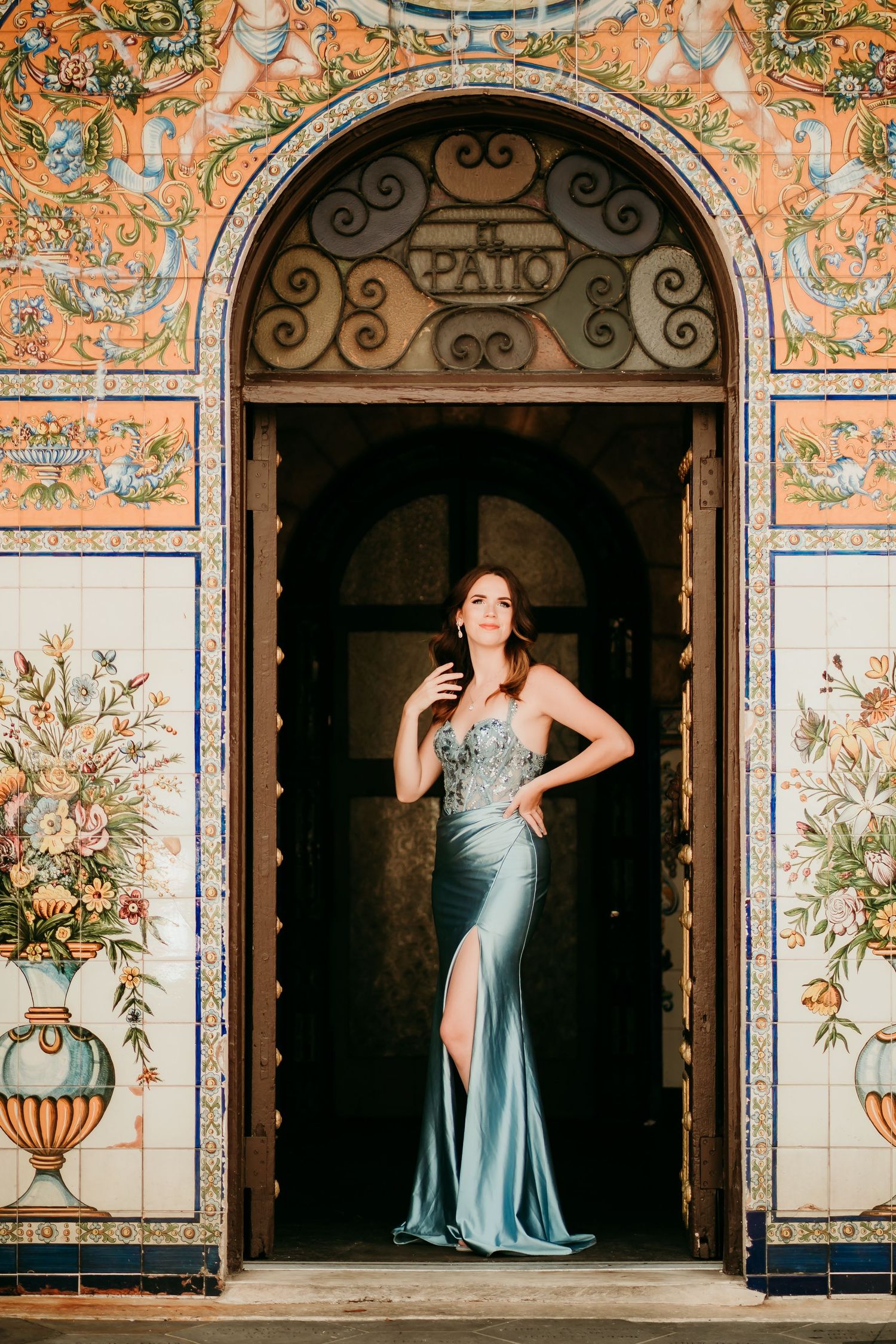 Woman in elegant teal gown posing in ornate tiled archway entrance at El Patio.