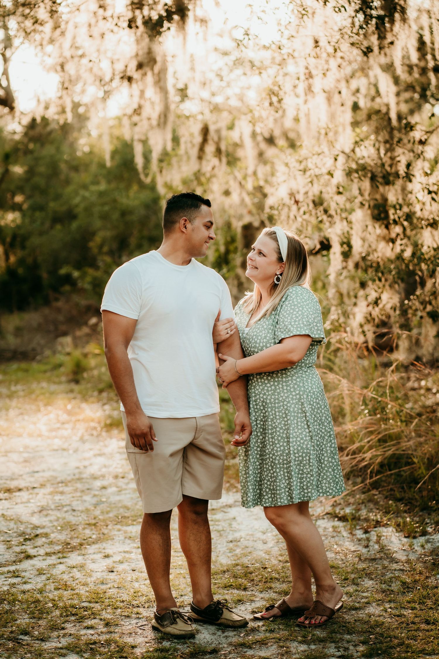 Couple holding hands and gazing at each other in sunlit forest.