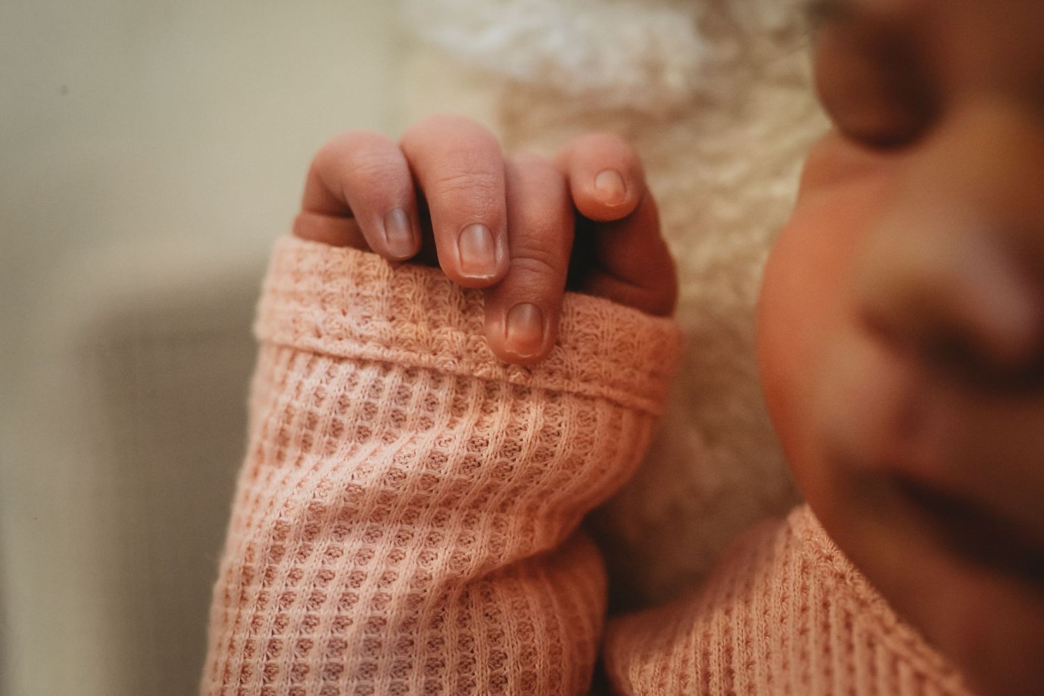 Close-up of newborn baby tiny fingers in pink knit onesie.