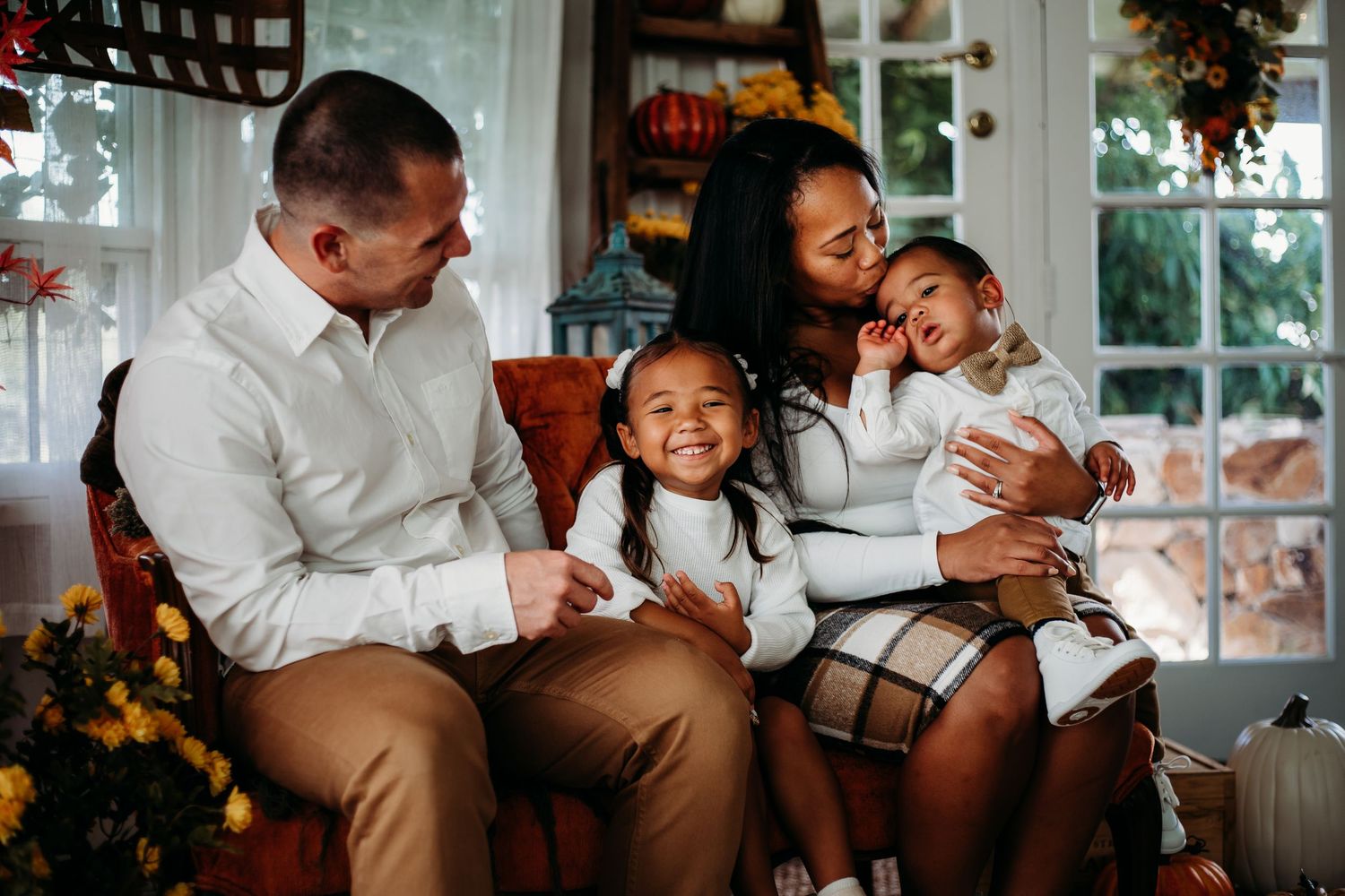Loving family of four sharing a warm moment together seated in a cozy fall-decorated home setting.