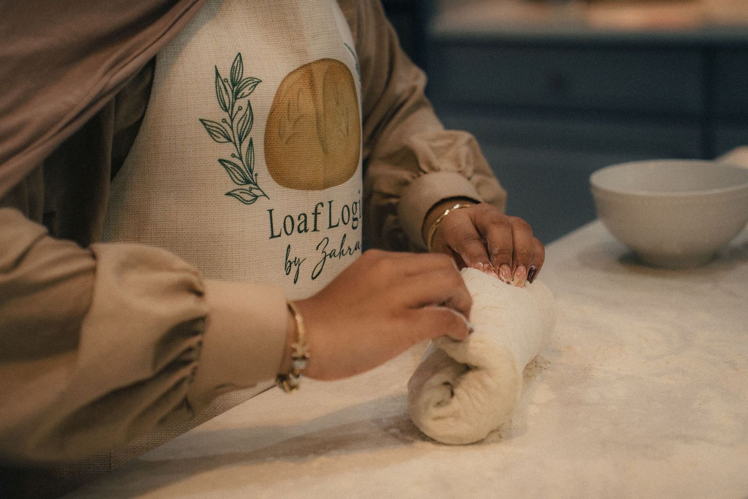 Baker kneading dough on floured surface wearing a Loaf Log by Julia branded apron.