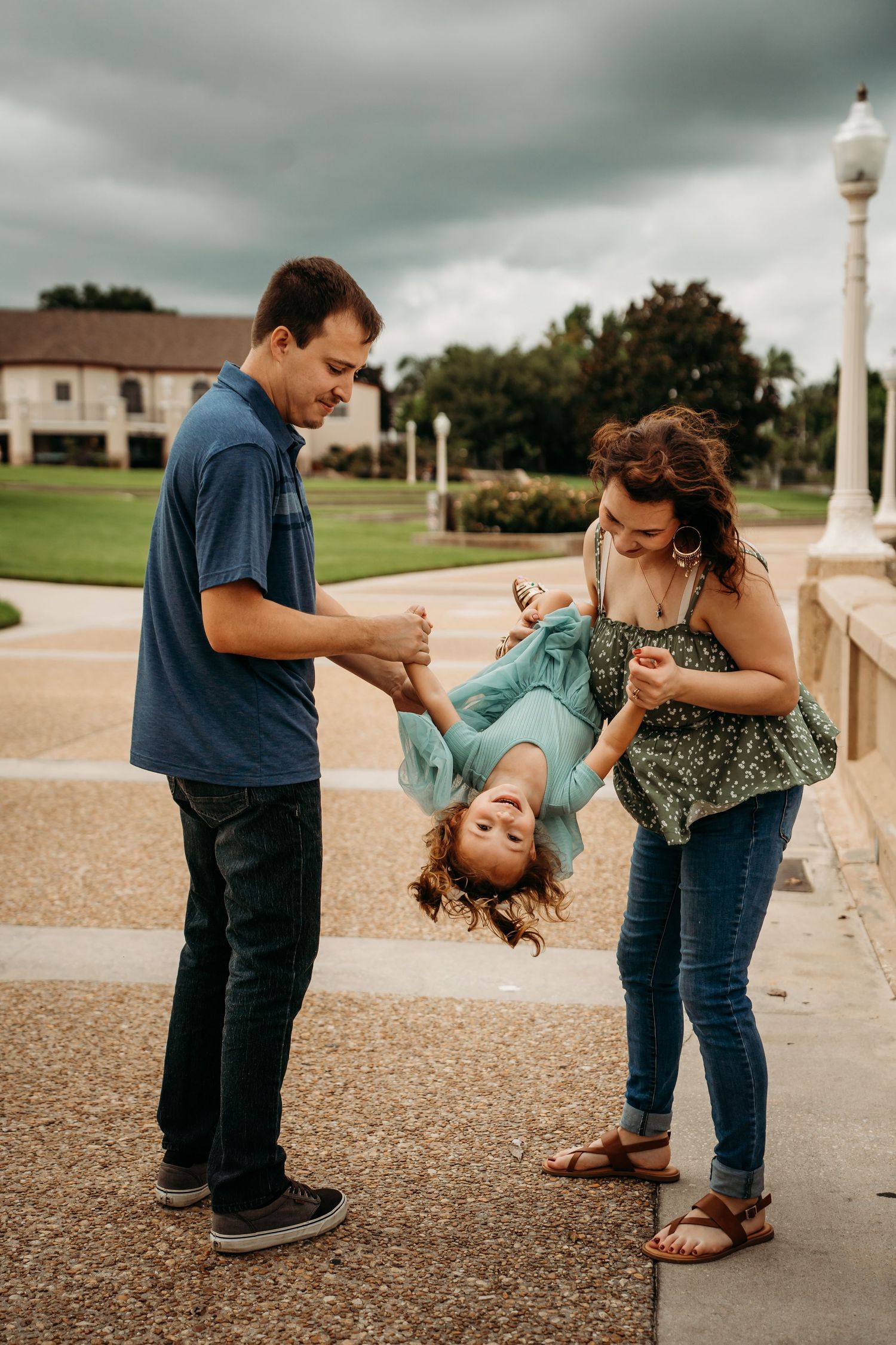 Parents playfully flip their laughing child upside down at an outdoor plaza.
