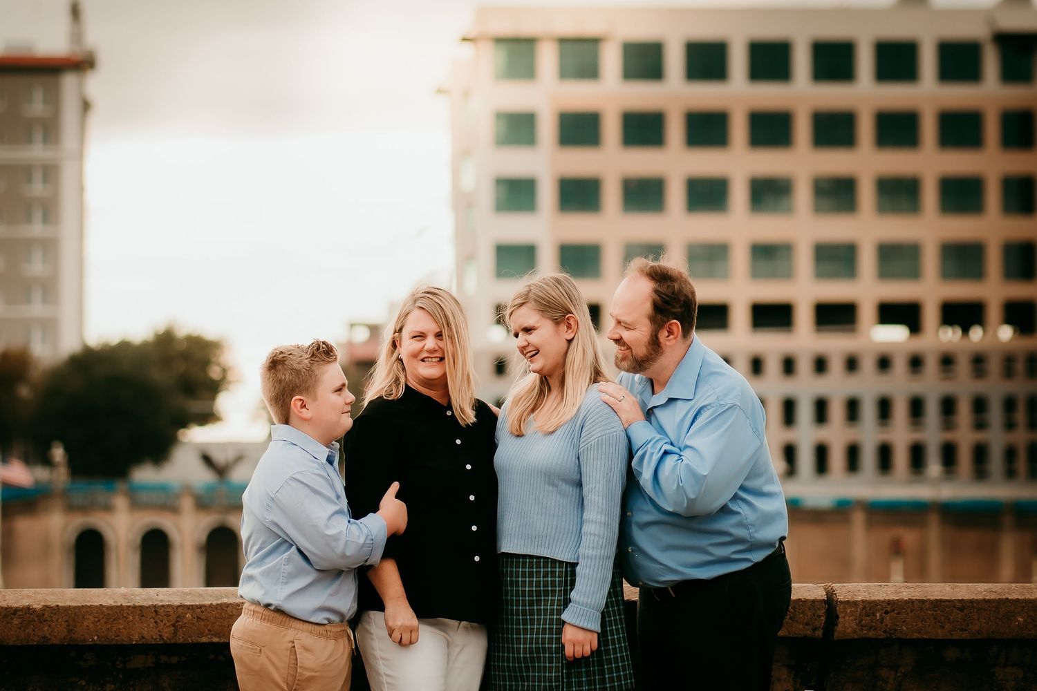 Cheerful family of four laughing together on an urban rooftop with city buildings behind.