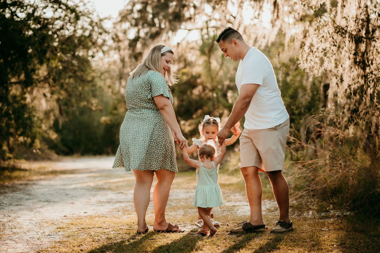 Family of four holding hands and walking together on a sunlit outdoor path.