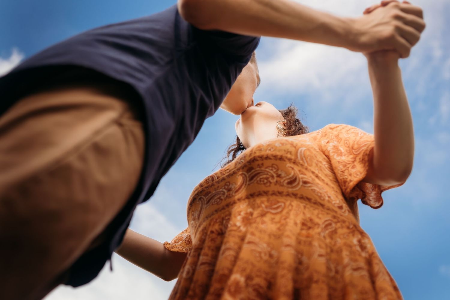 Low-angle view of a couple holding hands and dancing under a bright blue sky, captured from below.