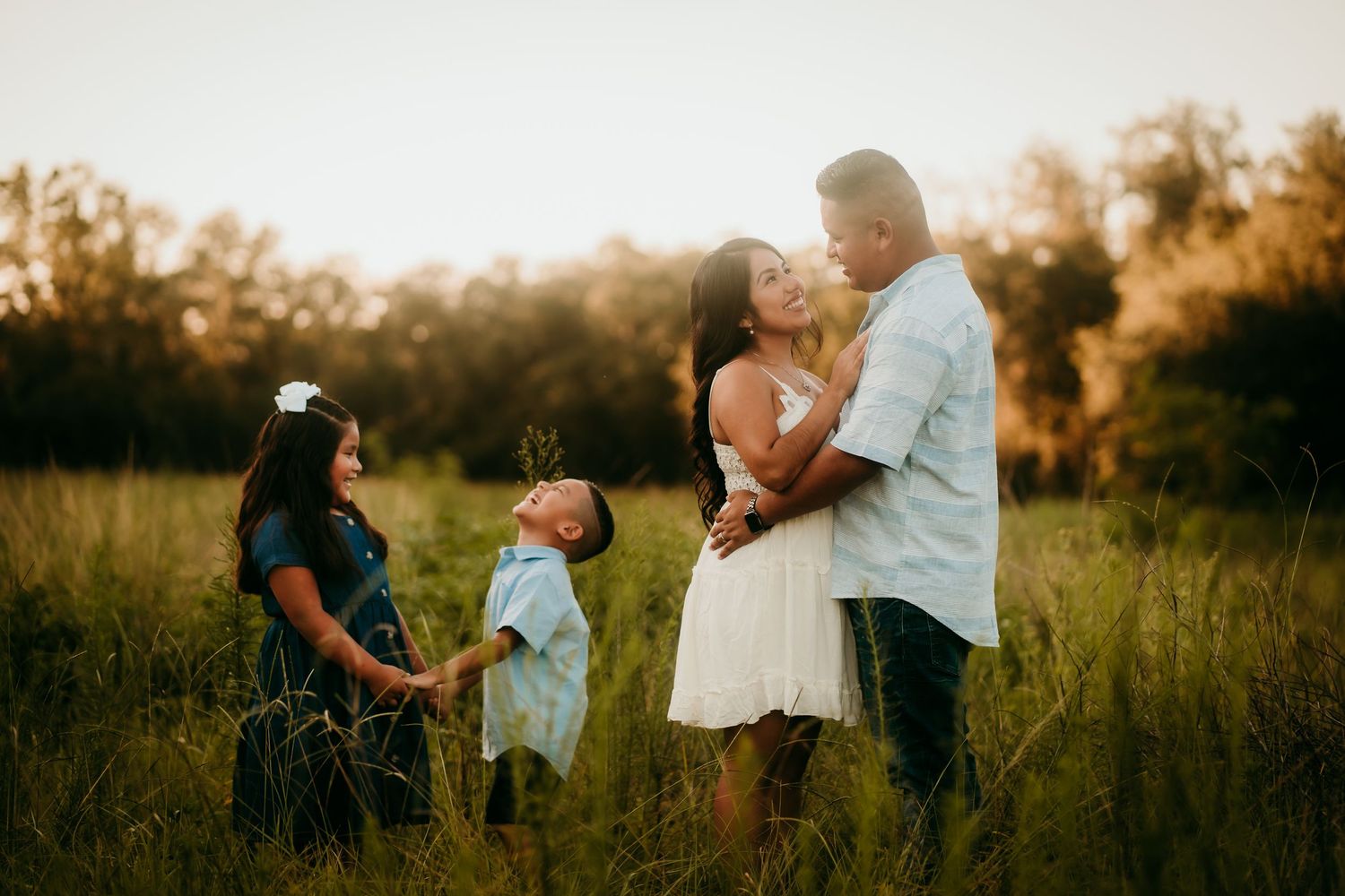 Romantic couple embracing in a golden meadow while their two children play nearby.