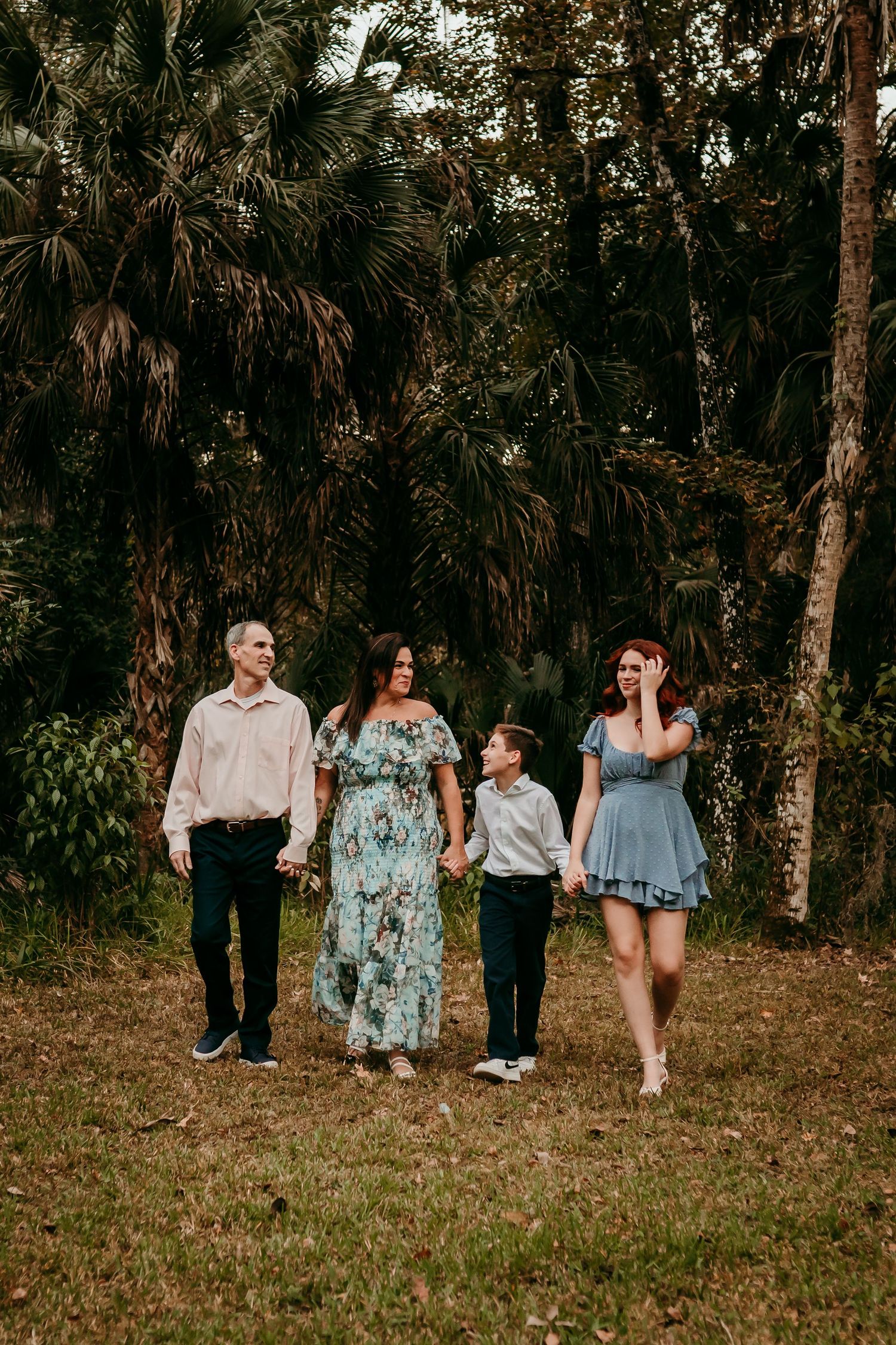 Family of four holding hands while walking through lush tropical park.