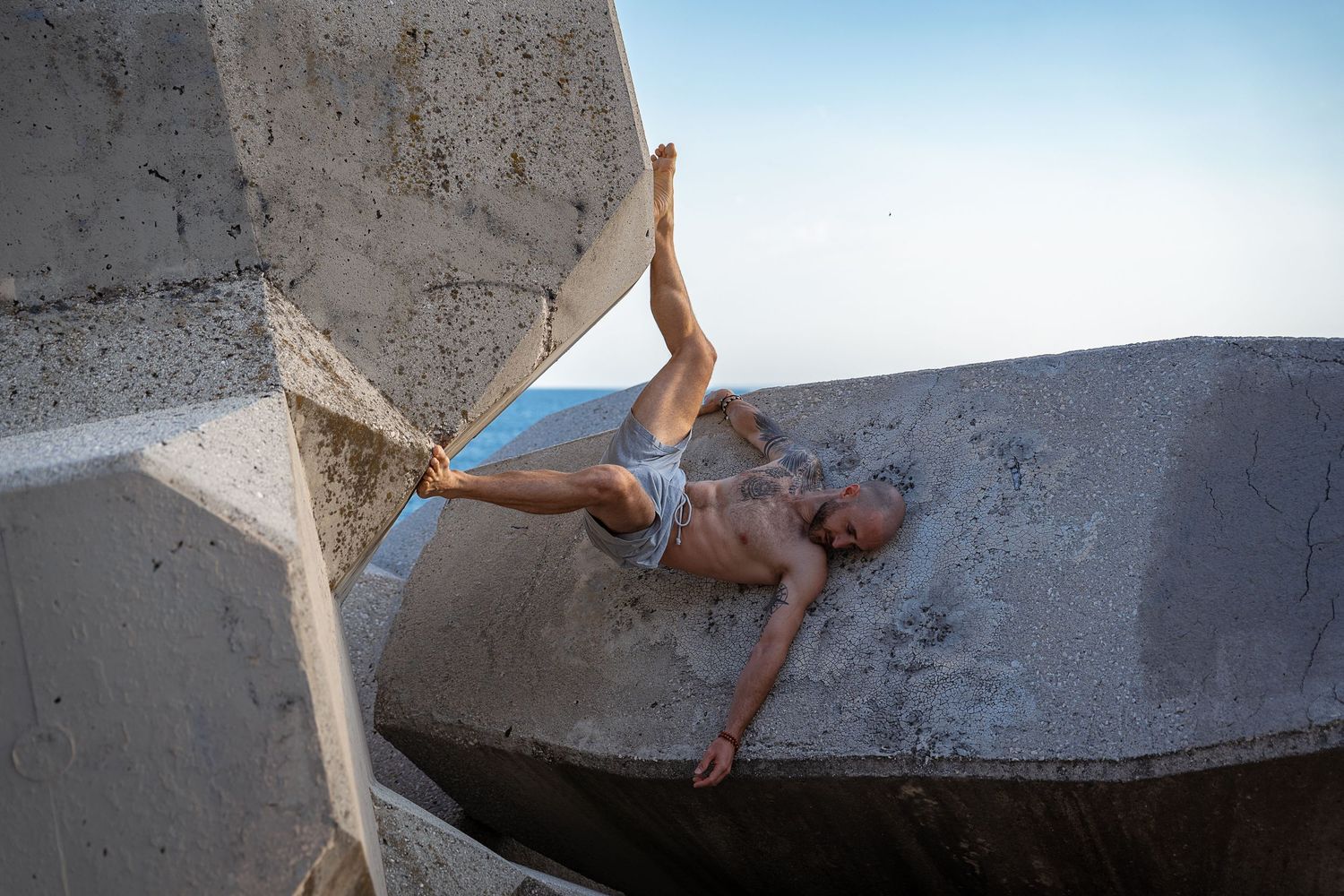 Shirtless bald man performing extreme parkour move on large concrete blocks outdoors.