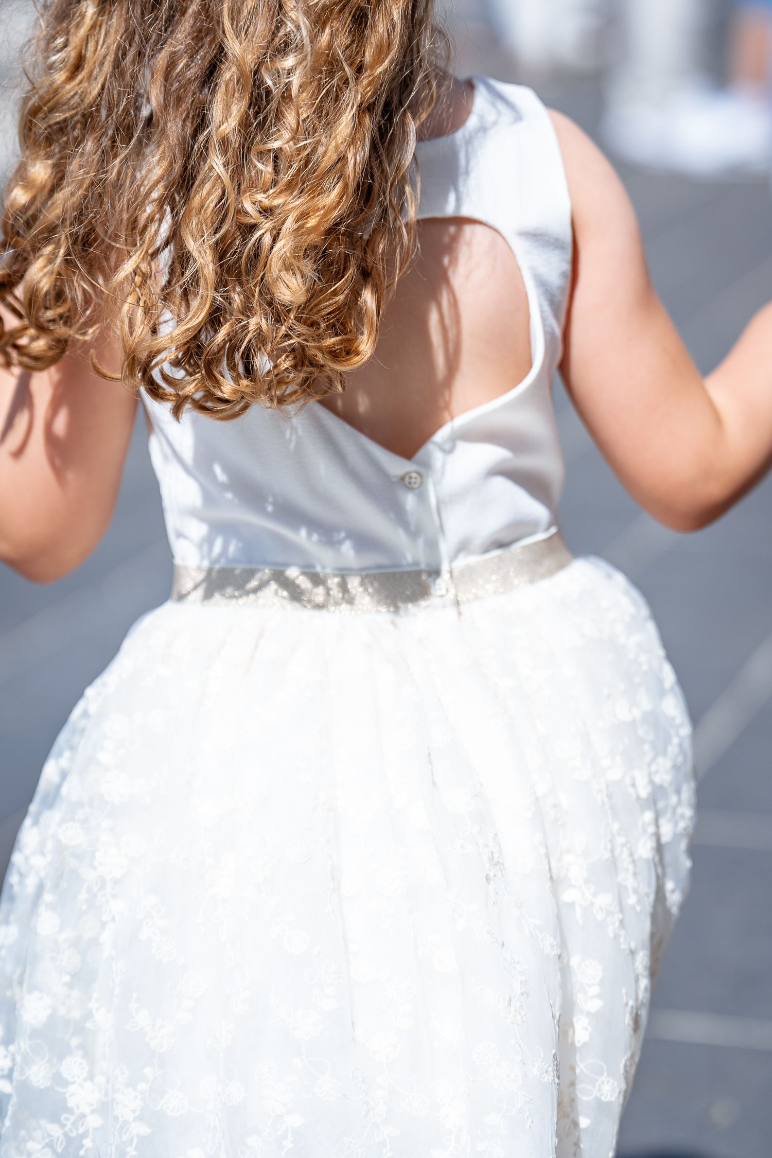 Back view of a young girl in a white floral tulle dress with curly hair in sunlight.