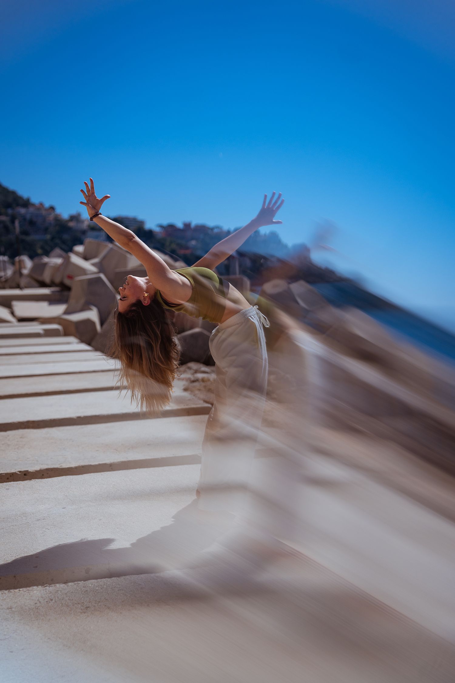 Long exposure motion blur of dancer performing expressive movement on coastal stone steps.