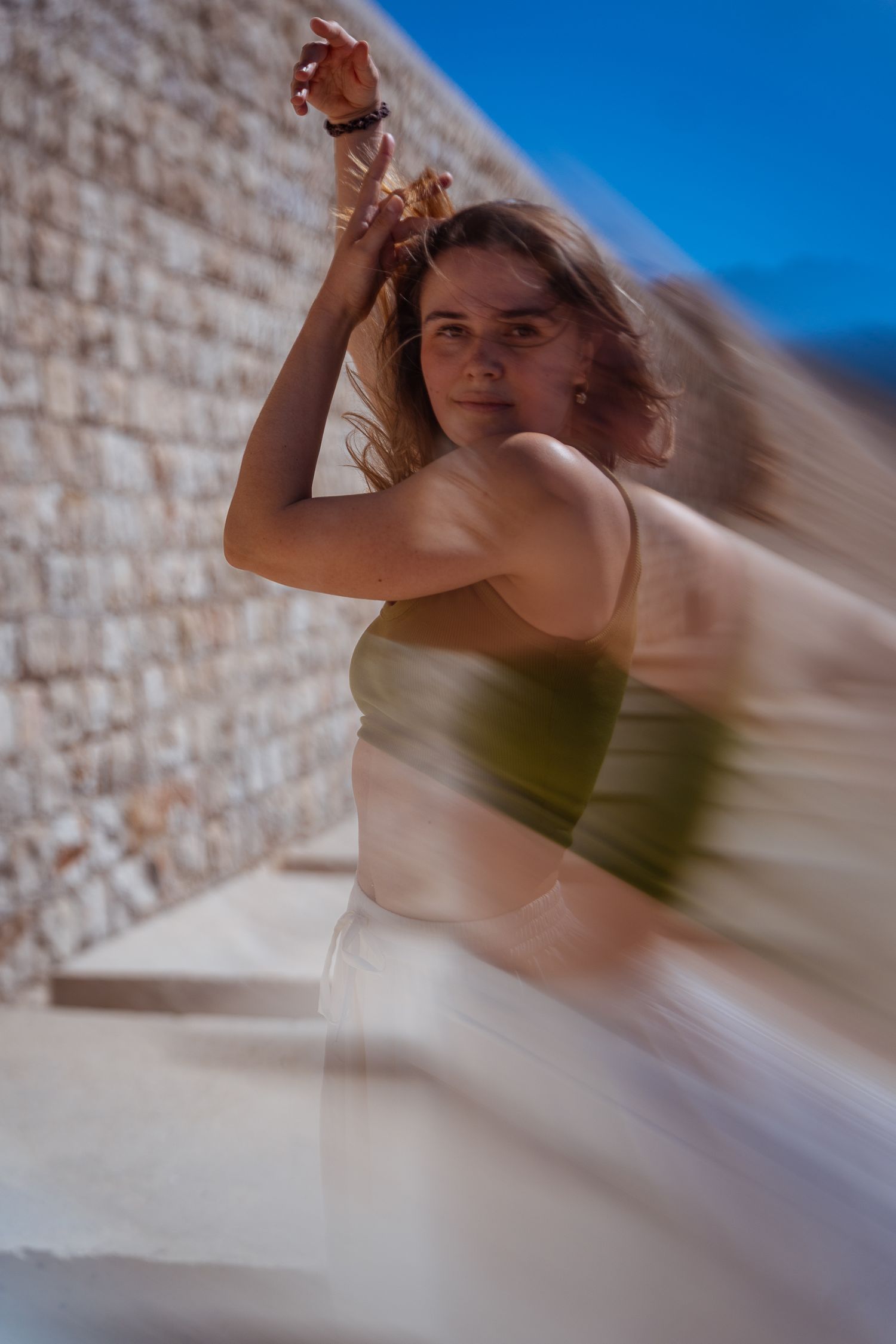 Young woman dancing outdoors with motion blur effect against stone wall.