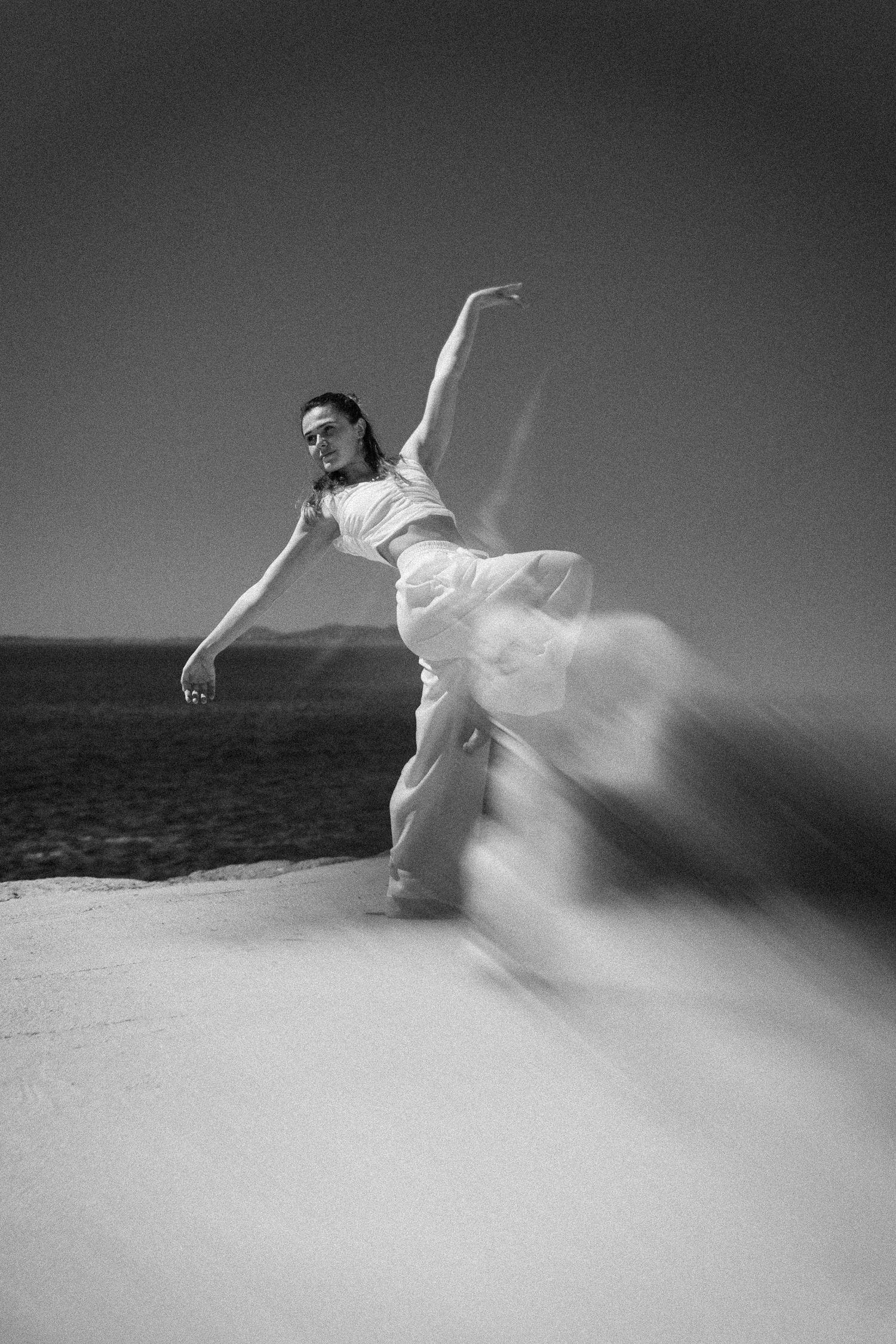 Black and white long exposure photo of dancer performing graceful movement by the sea.