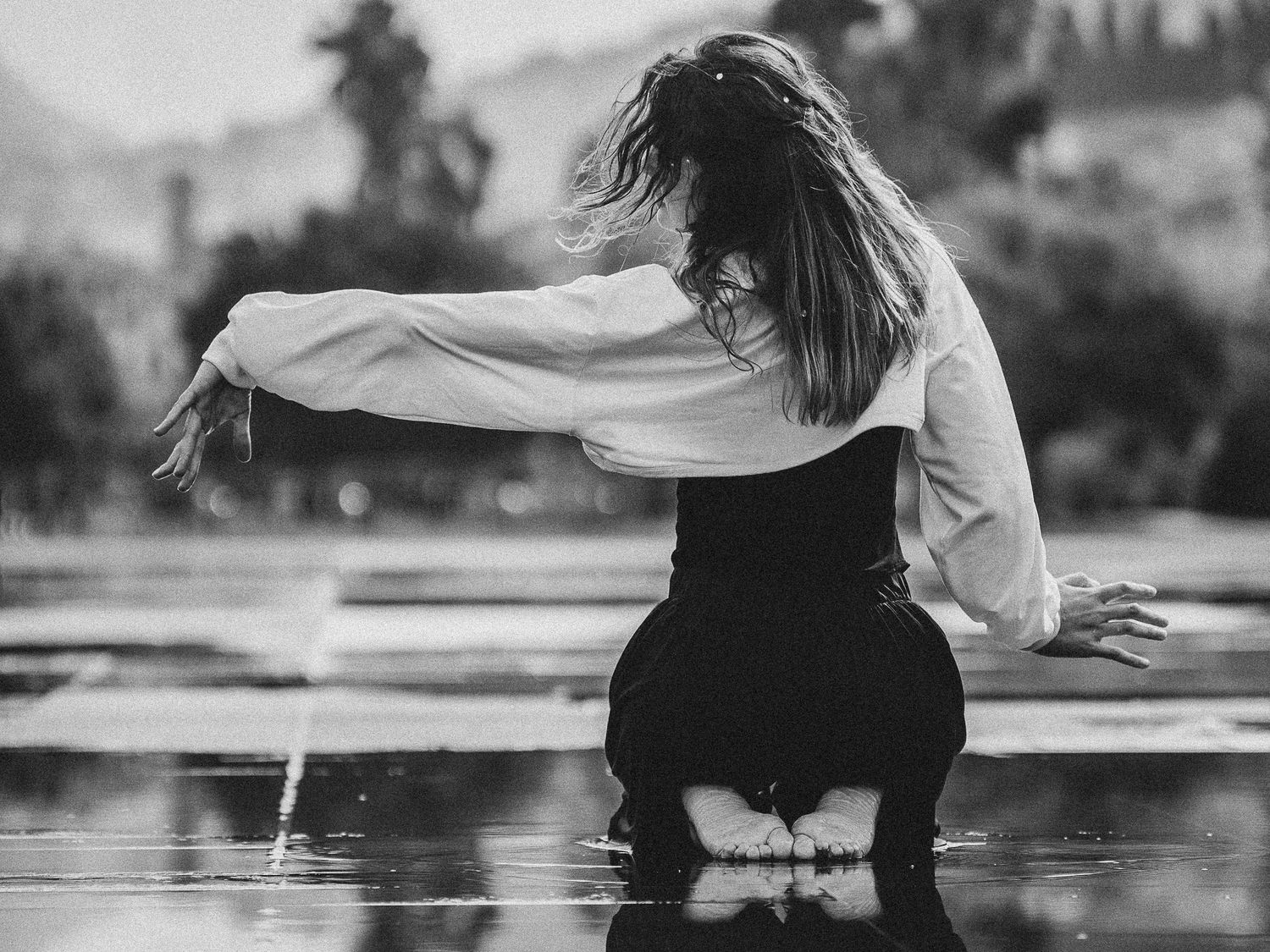 Black and white photo of woman kneeling on wet surface with hair and arms flowing dramatically.