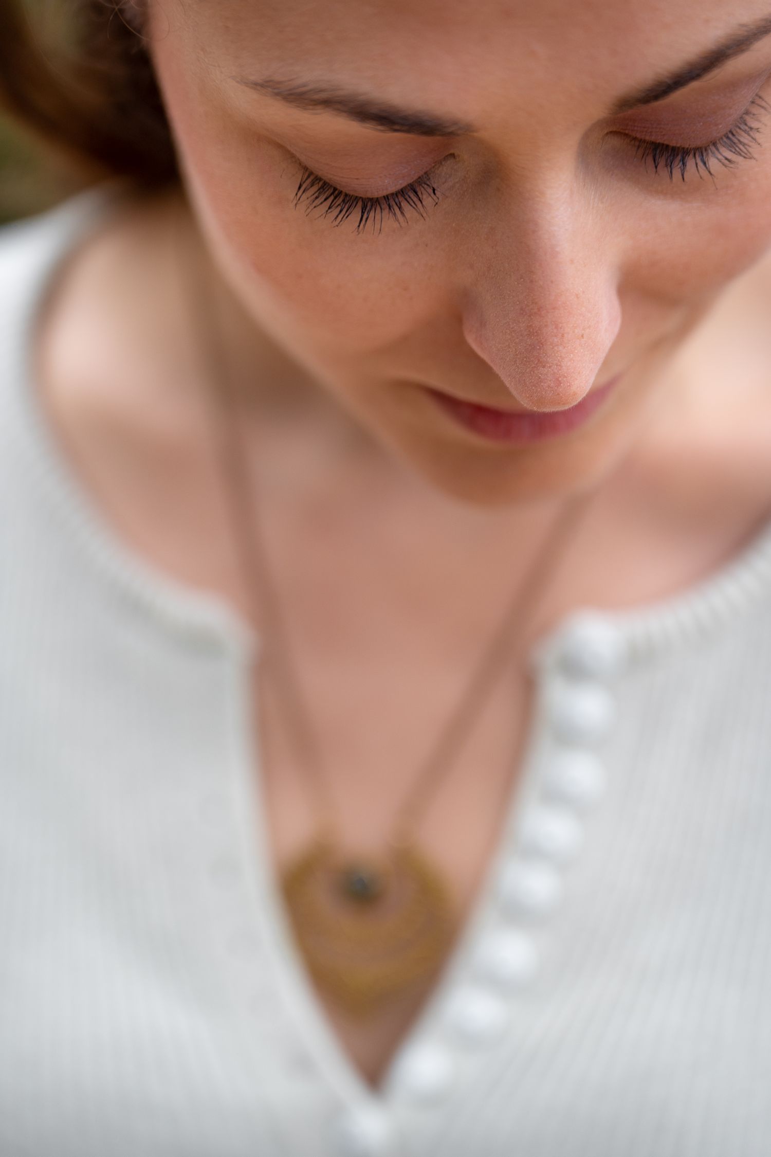 Close-up portrait of serene woman with closed eyes wearing white top and gold pendant necklace.