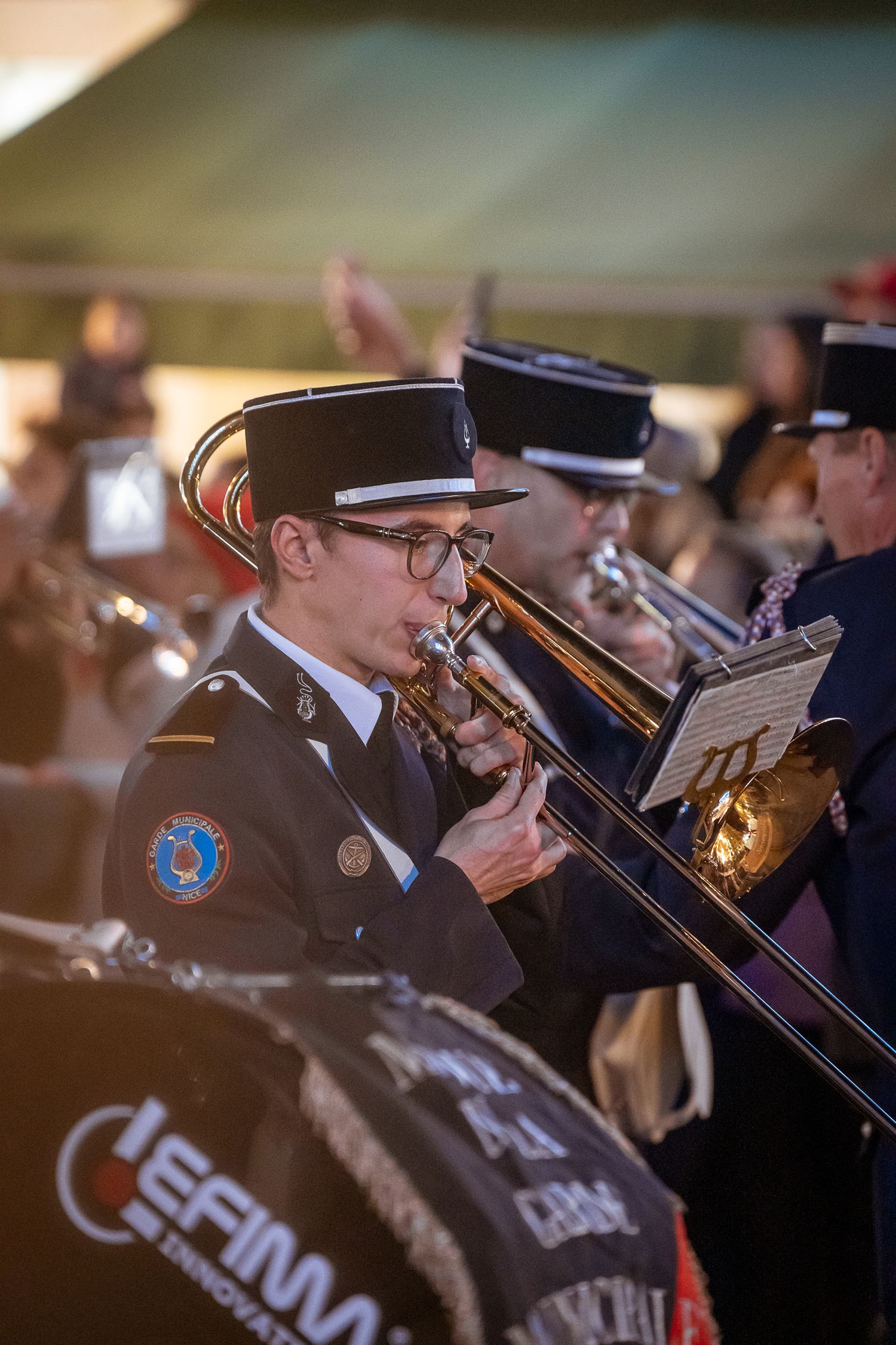 Young musician in military-style uniform playing trombone in an outdoor brass band performance.