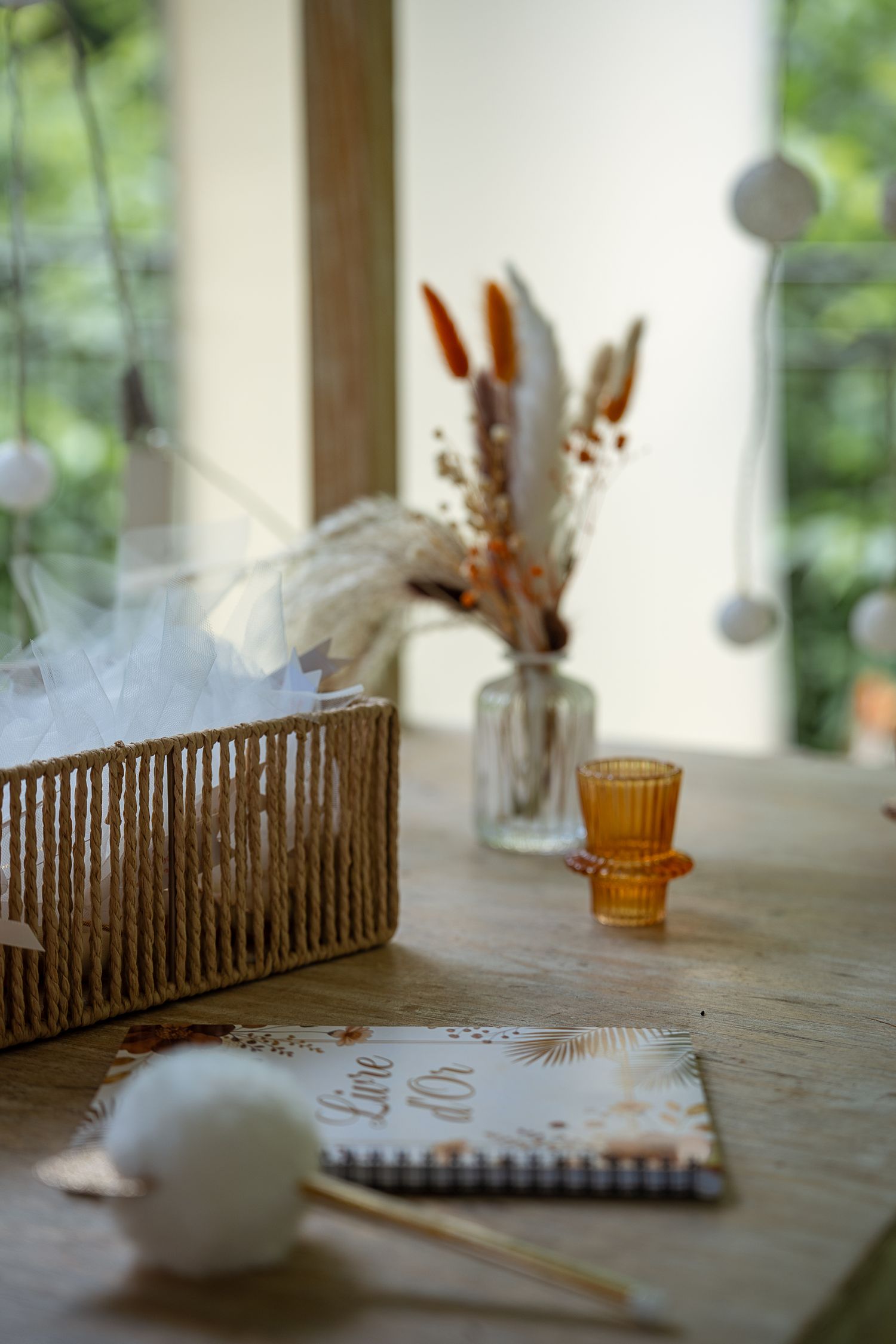Rustic wooden table with wicker basket, dried flowers in glass vase, and decorative notebook.