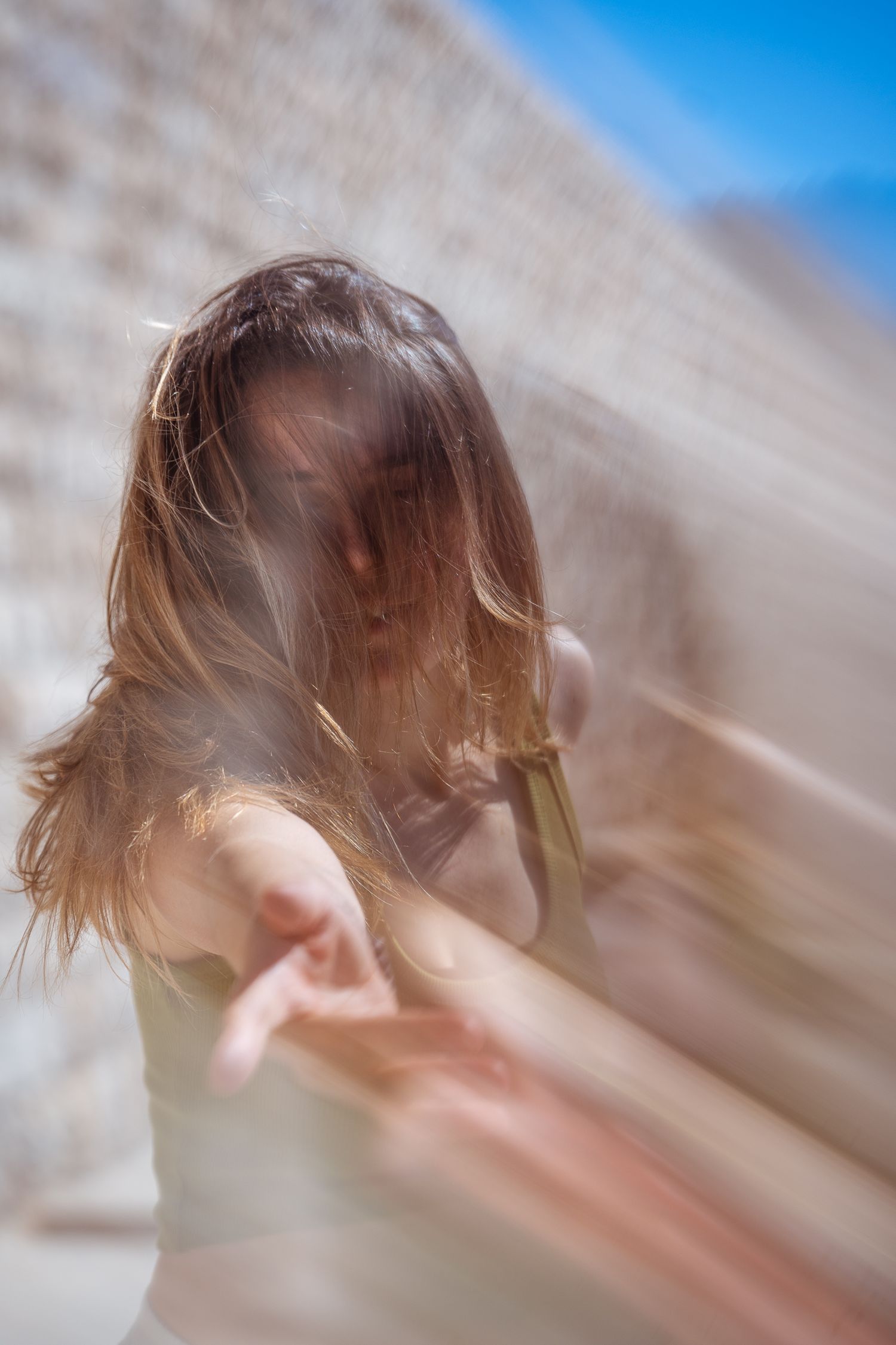Artistic motion blur portrait of woman with flowing hair reaching forward in sunlight.
