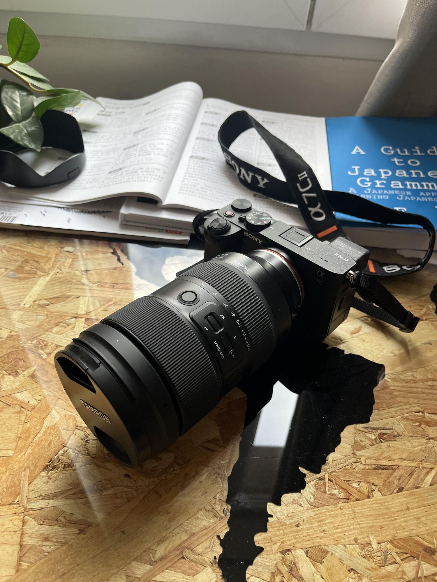 Sony mirrorless camera with large lens on wooden desk beside open grammar book.