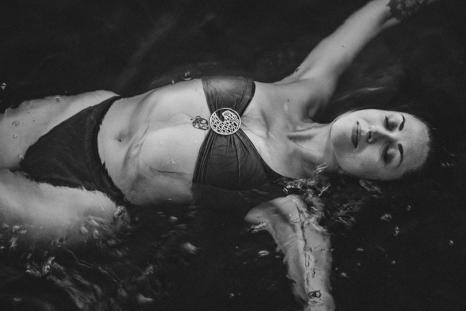 Black and white photo of woman in bikini floating in water with eyes closed.