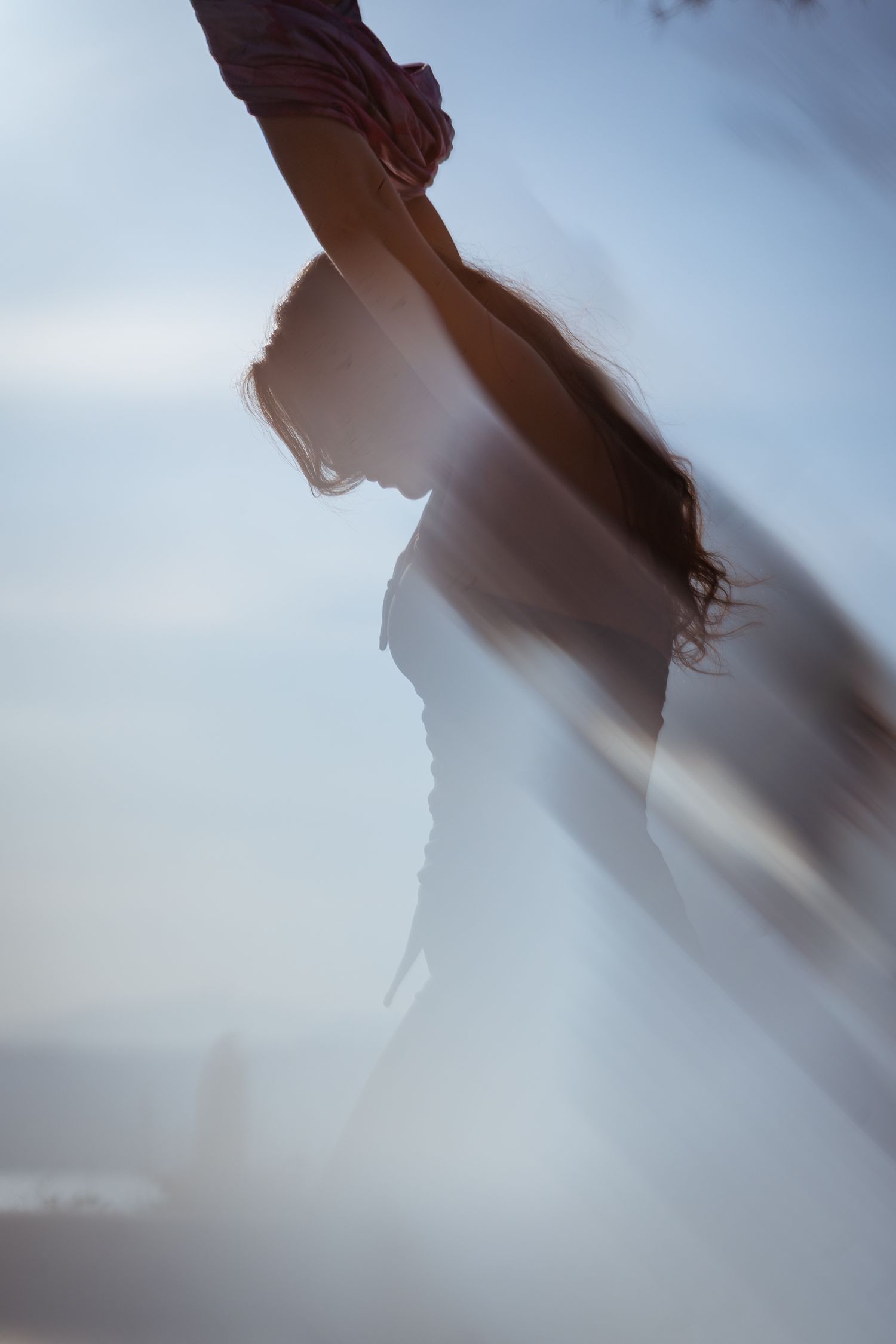 Dreamy double exposure silhouette of woman with long hair in soft blue light motion blur.