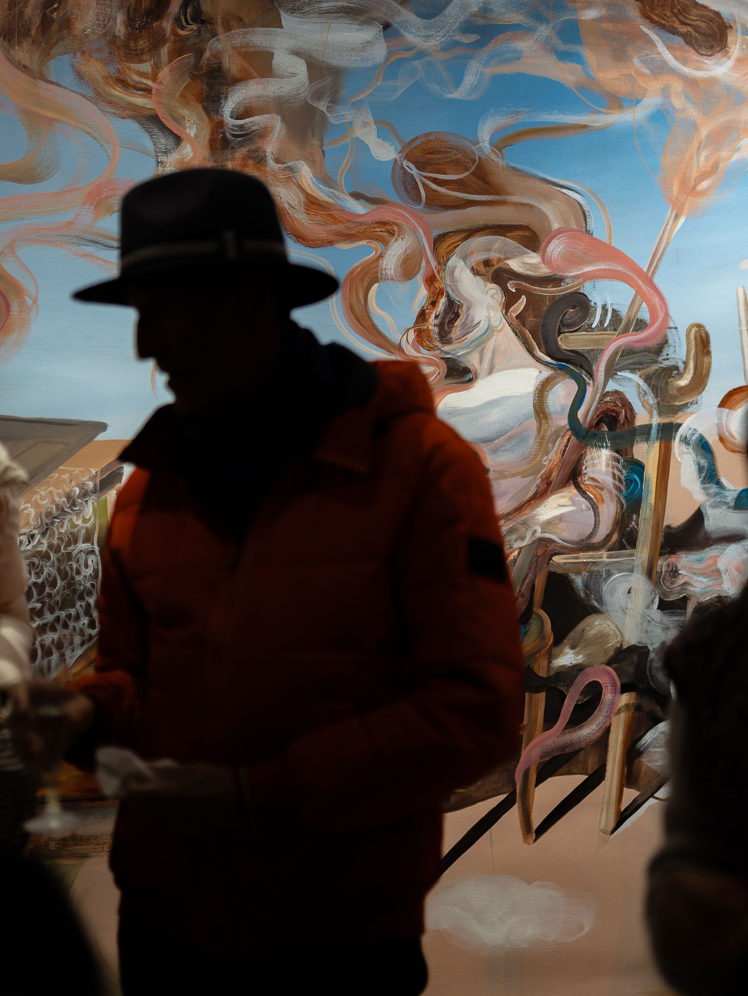 Silhouette of man in hat and orange jacket standing before colorful swirling abstract mural.
